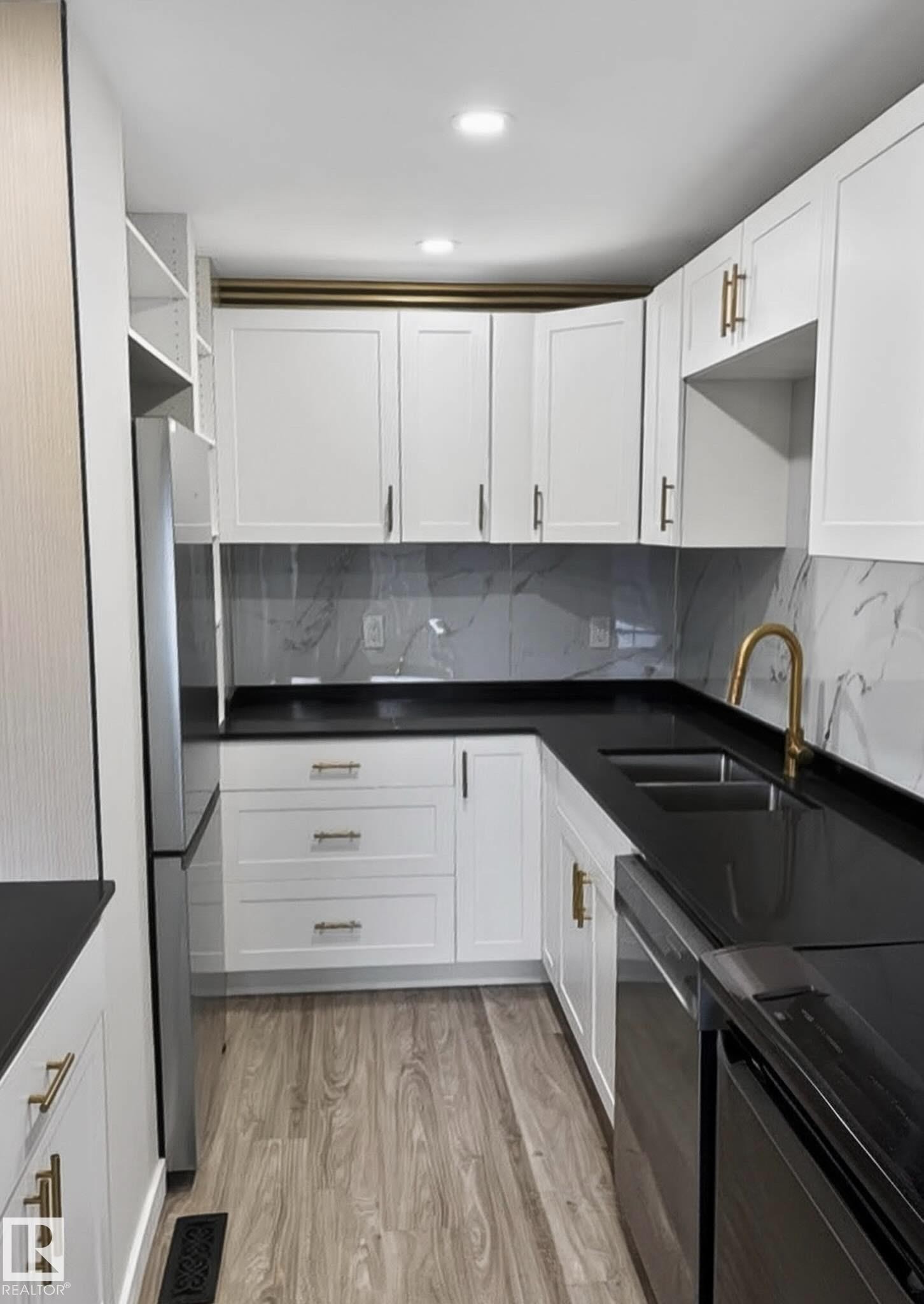 Kitchen featuring white shaker-style cabinetry, dark countertops, a light-toned wood-finish floor, and a patterned backsplash - 13833 24 Street W, Edmonton, AB - Indoor Photo Showing Kitchen With Double Sink