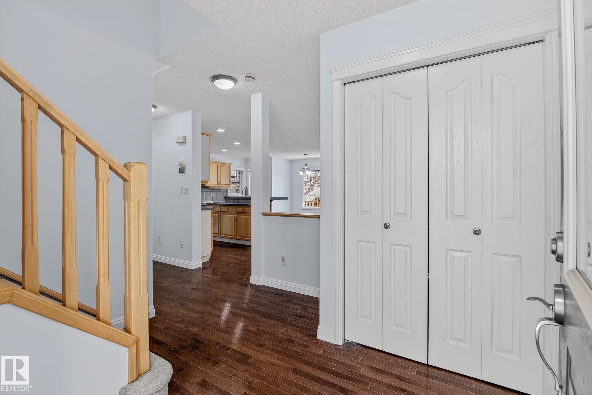 Entryway featuring wood-finish flooring, white bi-fold closet doors, a light wood staircase with carpeted treads, and a flush-mount ceiling light fixture - 978 Rutherford Road Sw, Edmonton, AB - Indoor Photo Showing Other Room