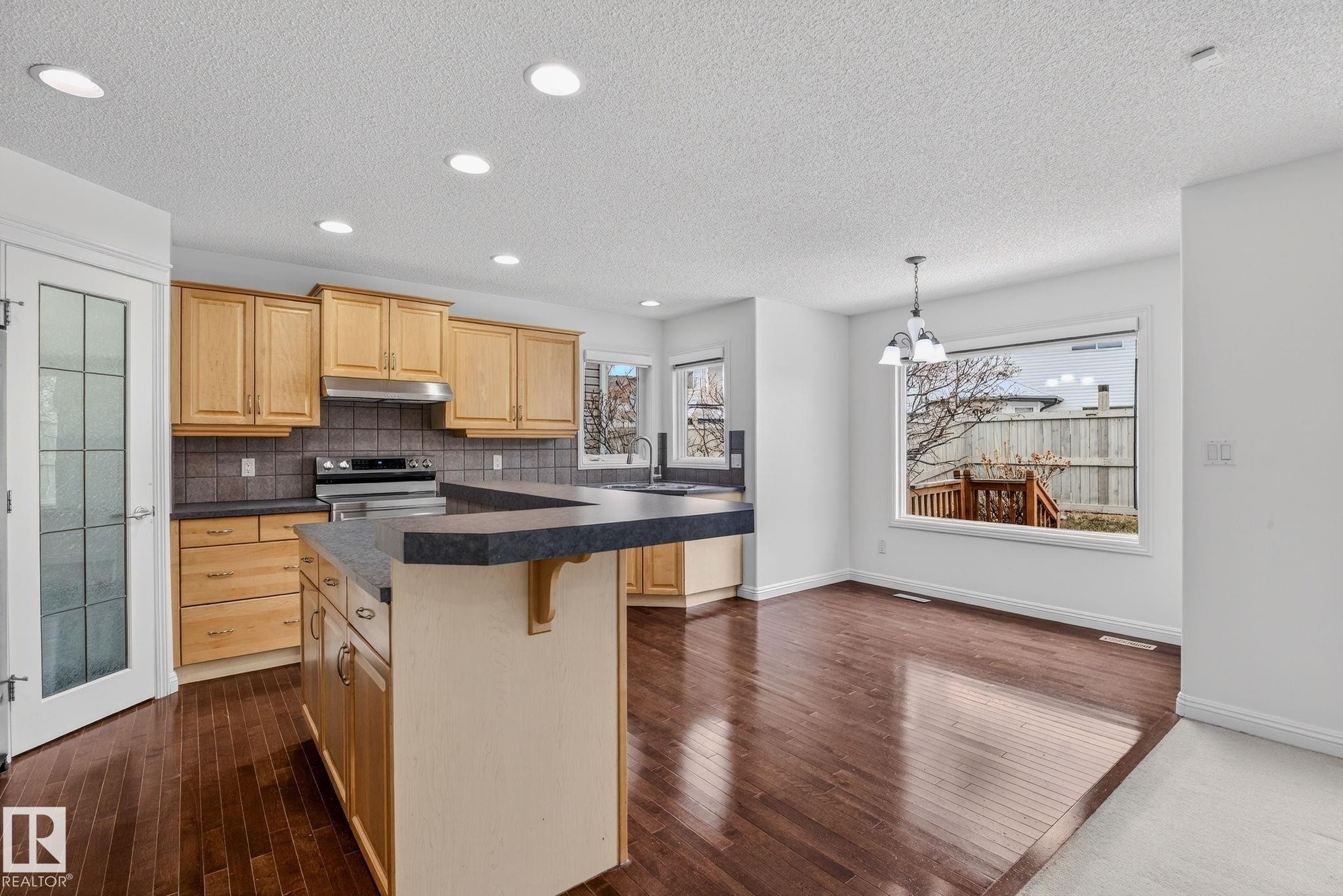 Open-concept kitchen and dining area featuring rich wood-finish flooring, light wood cabinetry, recessed lighting, and a kitchen island with seating - 978 Rutherford Road Sw, Edmonton, AB - Indoor Photo Showing Kitchen With Upgraded Kitchen