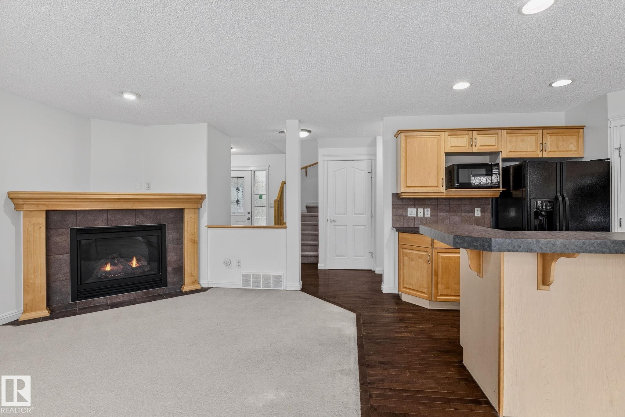 Living area featuring a gas fireplace with a wood mantle and dark tile surround - 978 Rutherford Road Sw, Edmonton, AB - Indoor With Fireplace