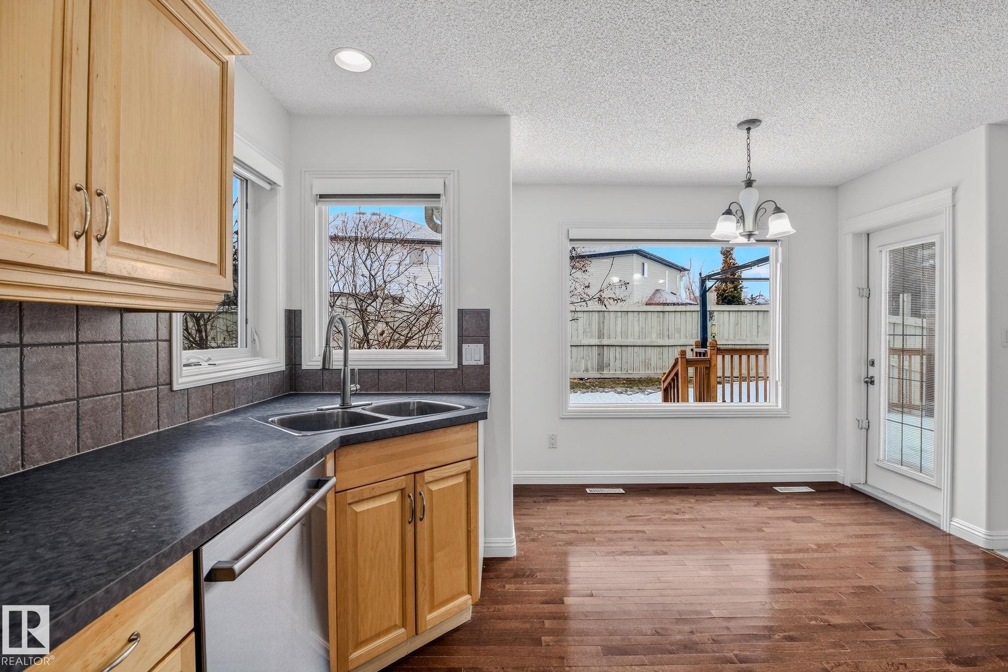 Kitchen featuring light wood cabinetry, dark countertops, and a tile backsplash - 978 Rutherford Road Sw, Edmonton, AB - Indoor Photo Showing Kitchen With Double Sink