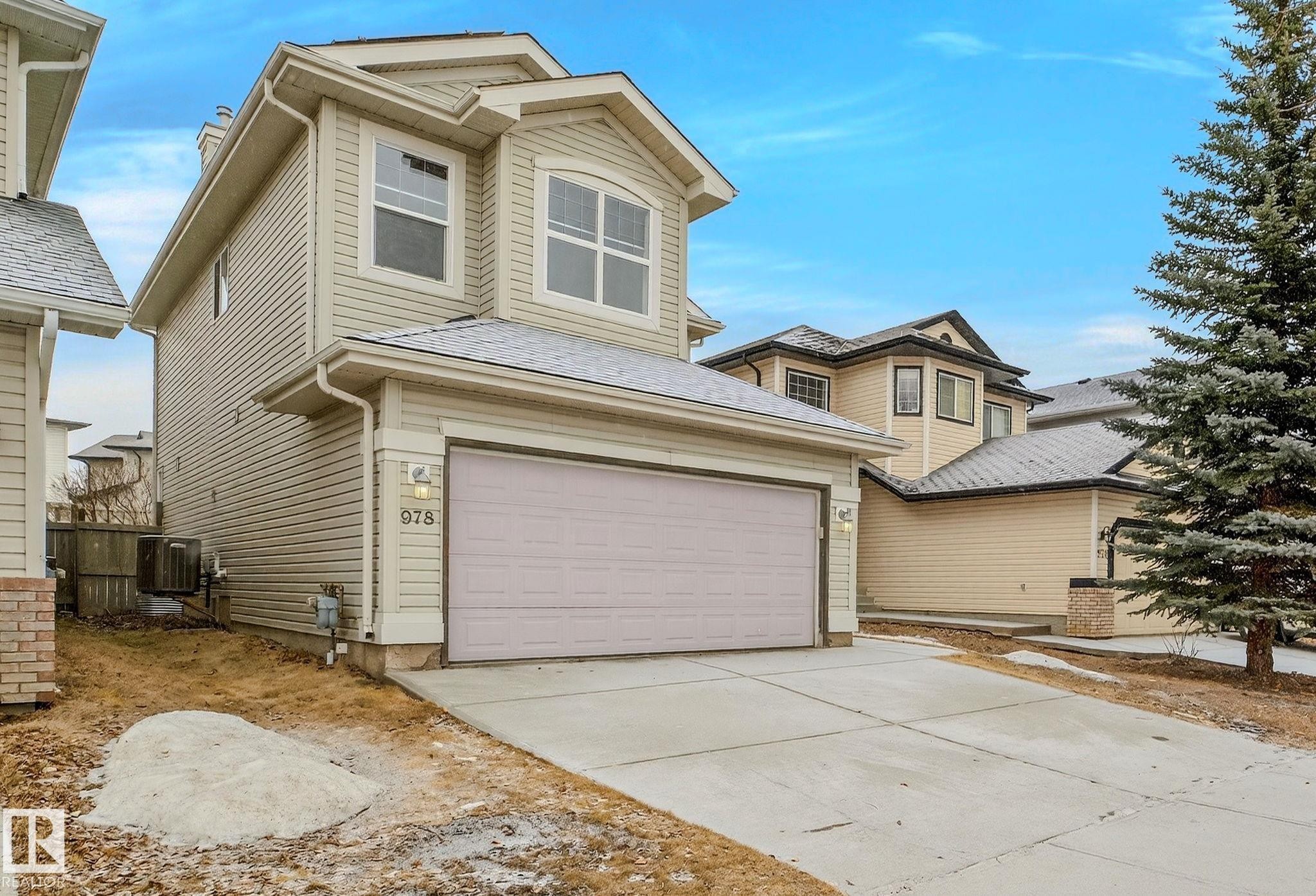 Two-story residence featuring light-toned horizontal siding, an attached garage with a concrete driveway, and a prominent arched window on the upper level - 978 Rutherford Road Sw, Edmonton, AB - Outdoor