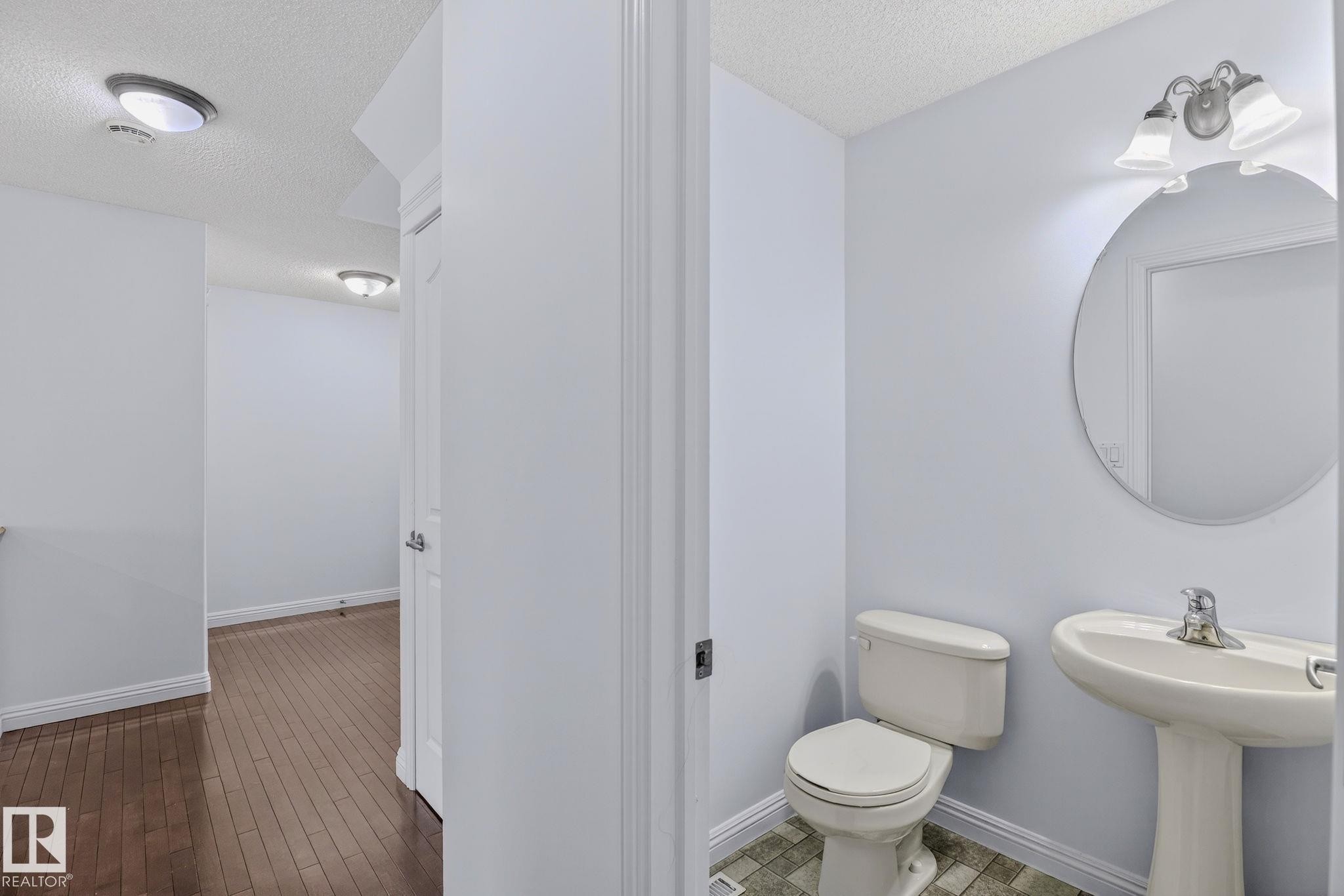Pedestal sink with single-handle faucet, circular mirror, and two-light vanity fixture - 978 Rutherford Road Sw, Edmonton, AB - Indoor Photo Showing Bathroom