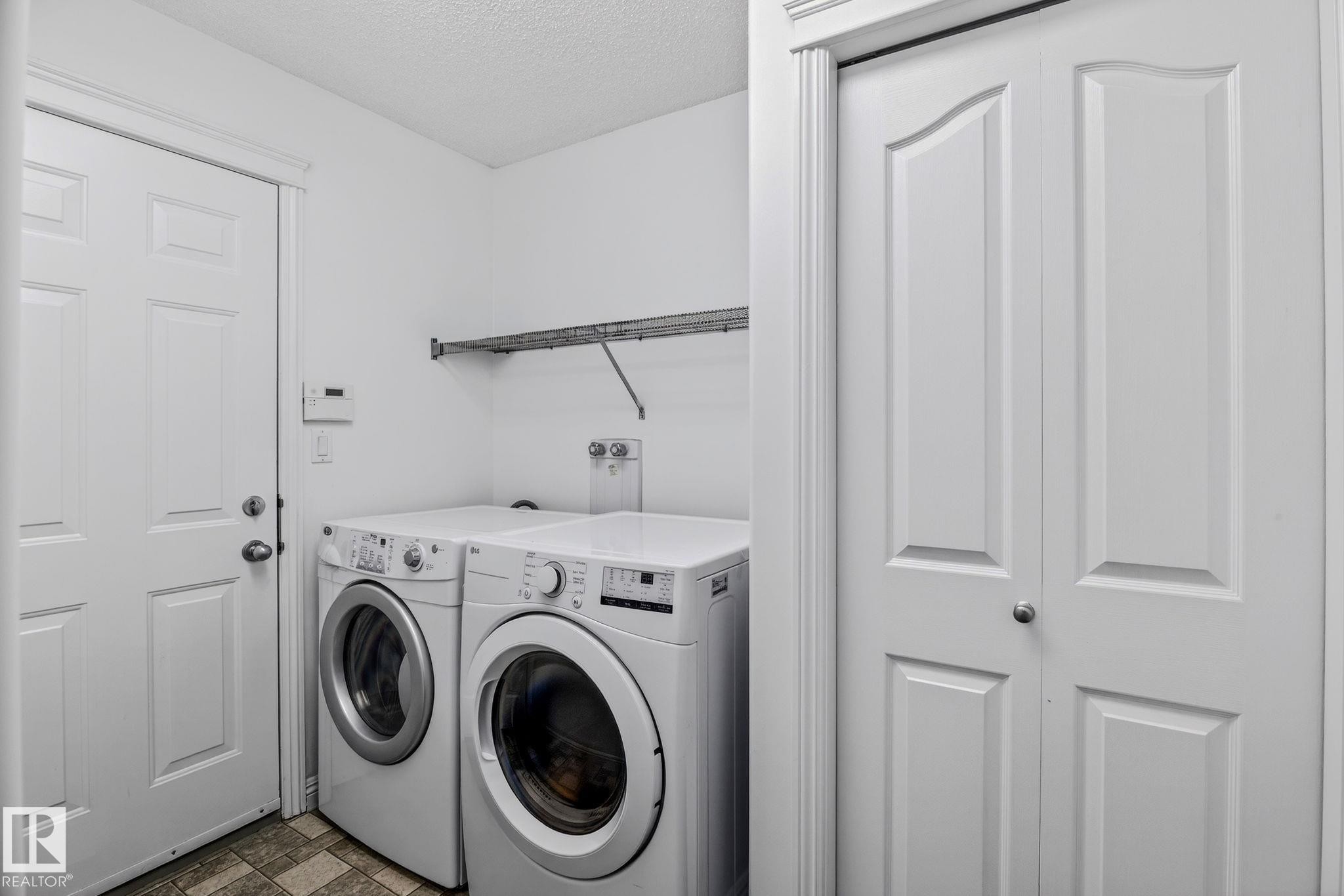 Dedicated utility space featuring a front-loading washer and dryer, a wire shelving unit, a paneled door, and a bi-fold door - 978 Rutherford Road Sw, Edmonton, AB - Indoor Photo Showing Laundry Room