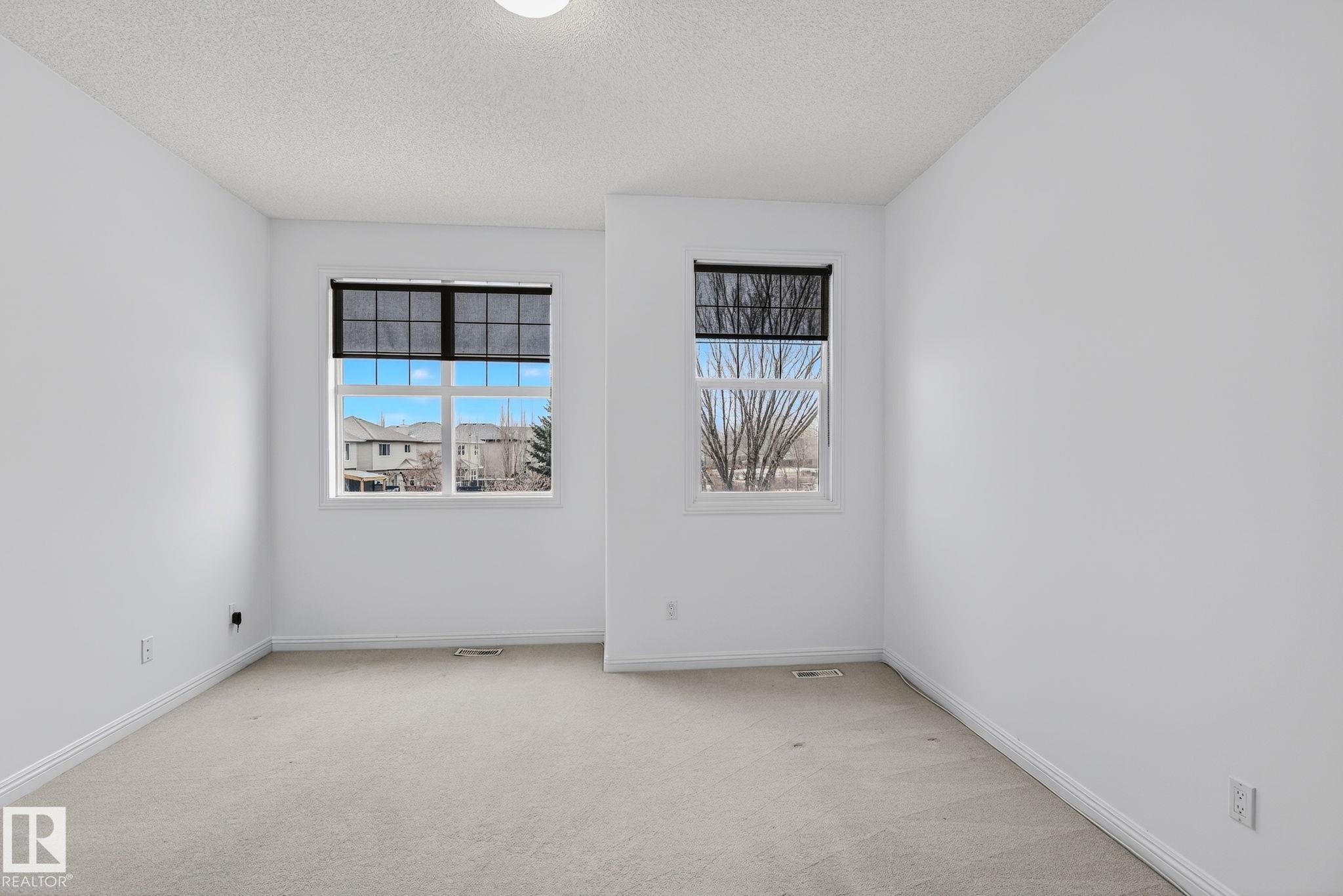 Bright interior space featuring two windows with roller shades, light grey carpet flooring, white painted walls, and white trim molding - 978 Rutherford Road Sw, Edmonton, AB - Indoor Photo Showing Other Room