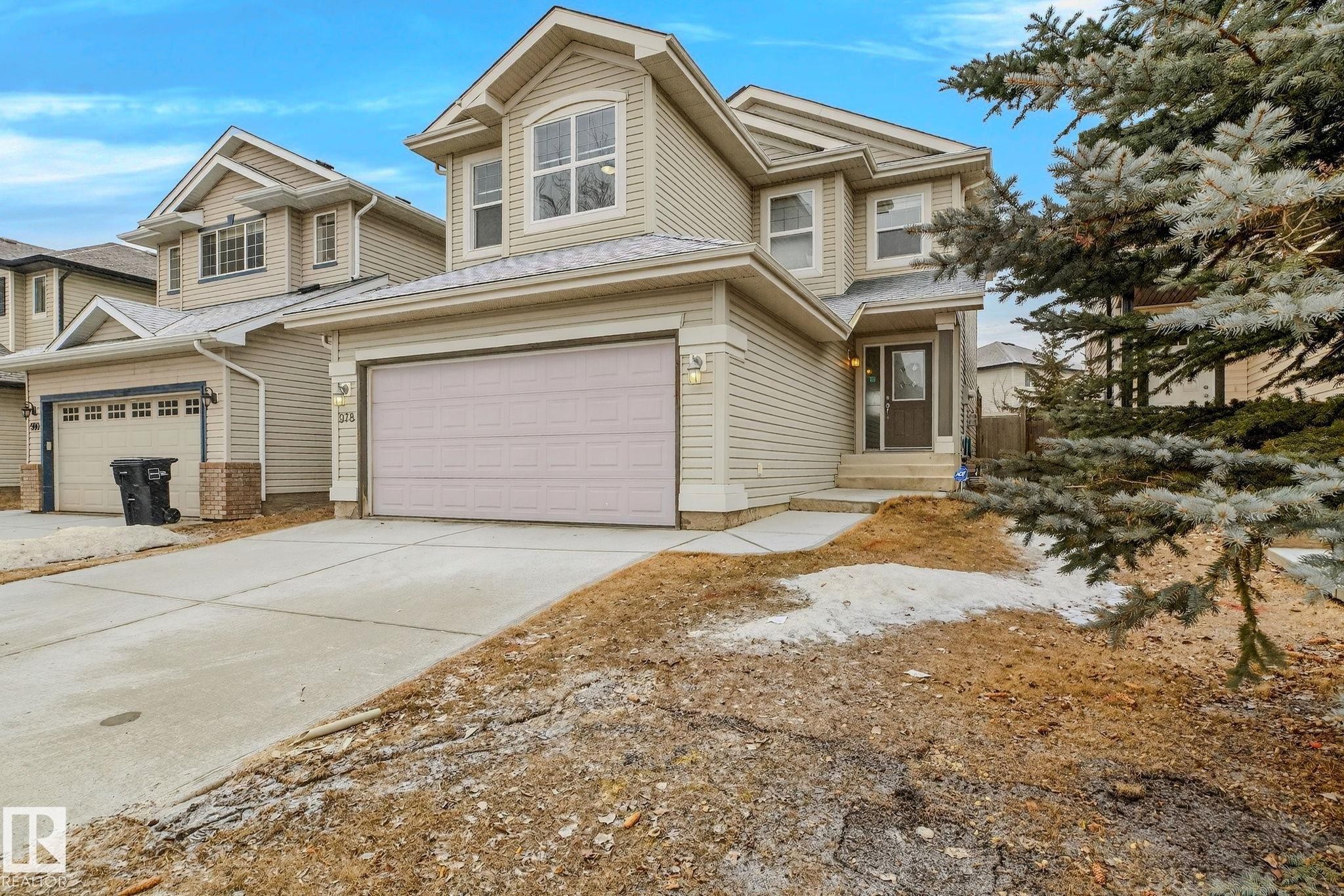 Two-story residence featuring light-colored siding, an attached double garage with a panel door, and a concrete driveway - 978 Rutherford Road Sw, Edmonton, AB - Outdoor With Facade
