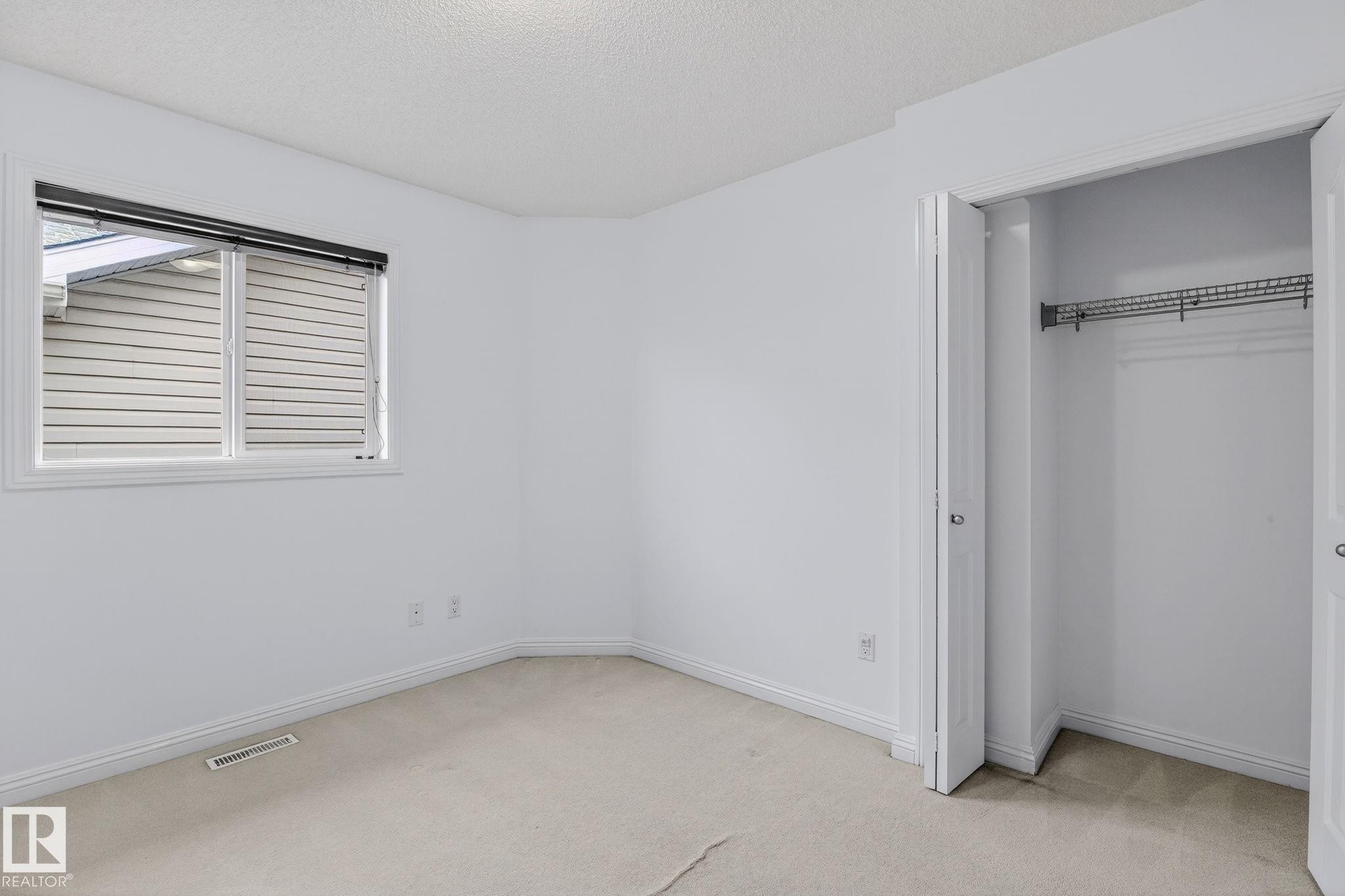 Carpeted room featuring a double-door closet with wire shelving, a window with horizontal blinds, white baseboards, and a ceiling with a textured finish - 978 Rutherford Road Sw, Edmonton, AB - Indoor Photo Showing Other Room