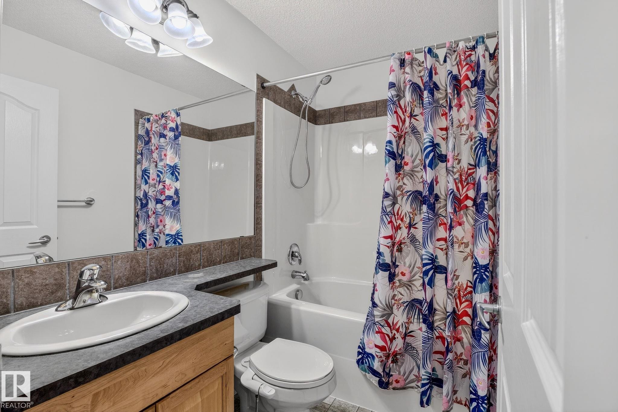 Bathroom featuring a wood-finish vanity with an integrated sink, a dark countertop, and a full-width mirror - 978 Rutherford Road Sw, Edmonton, AB - Indoor Photo Showing Bathroom