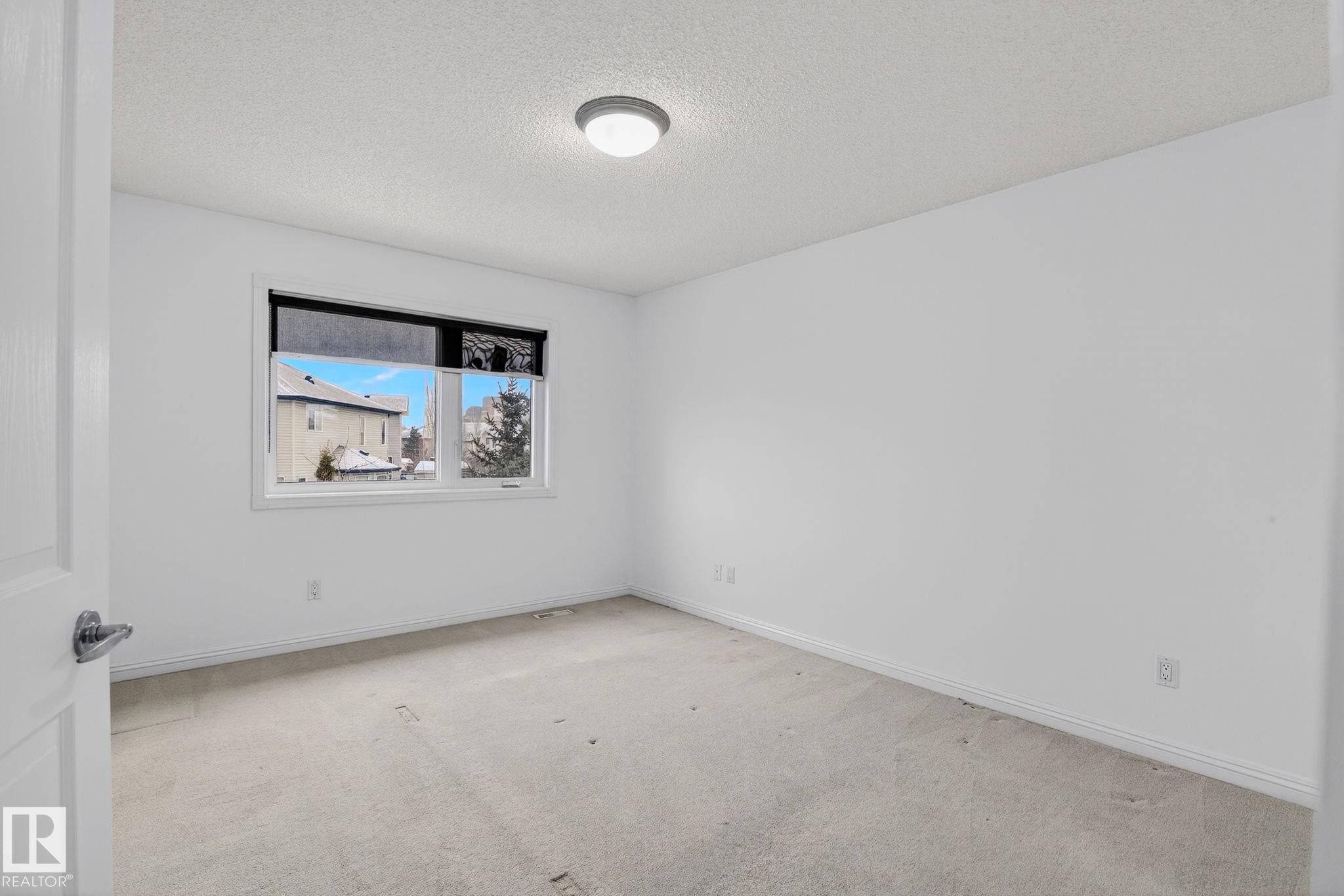 Spacious room featuring a large window, light-toned carpeting, white walls, and a ceiling-mounted light fixture - 978 Rutherford Road Sw, Edmonton, AB - Indoor Photo Showing Other Room