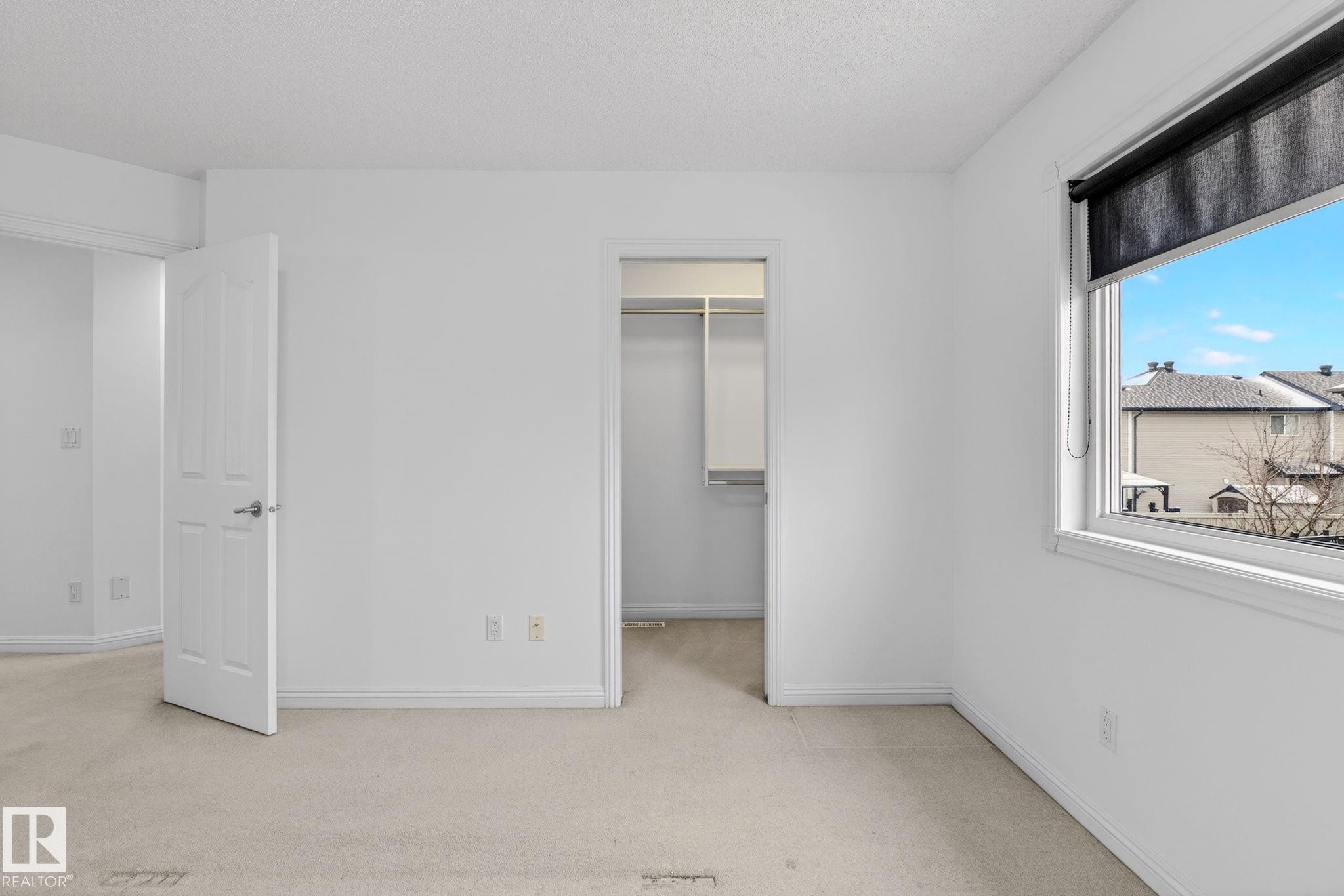 Bedroom featuring neutral carpeting, white walls, white trim, and a window with a roller shade - 978 Rutherford Road Sw, Edmonton, AB - Indoor Photo Showing Other Room