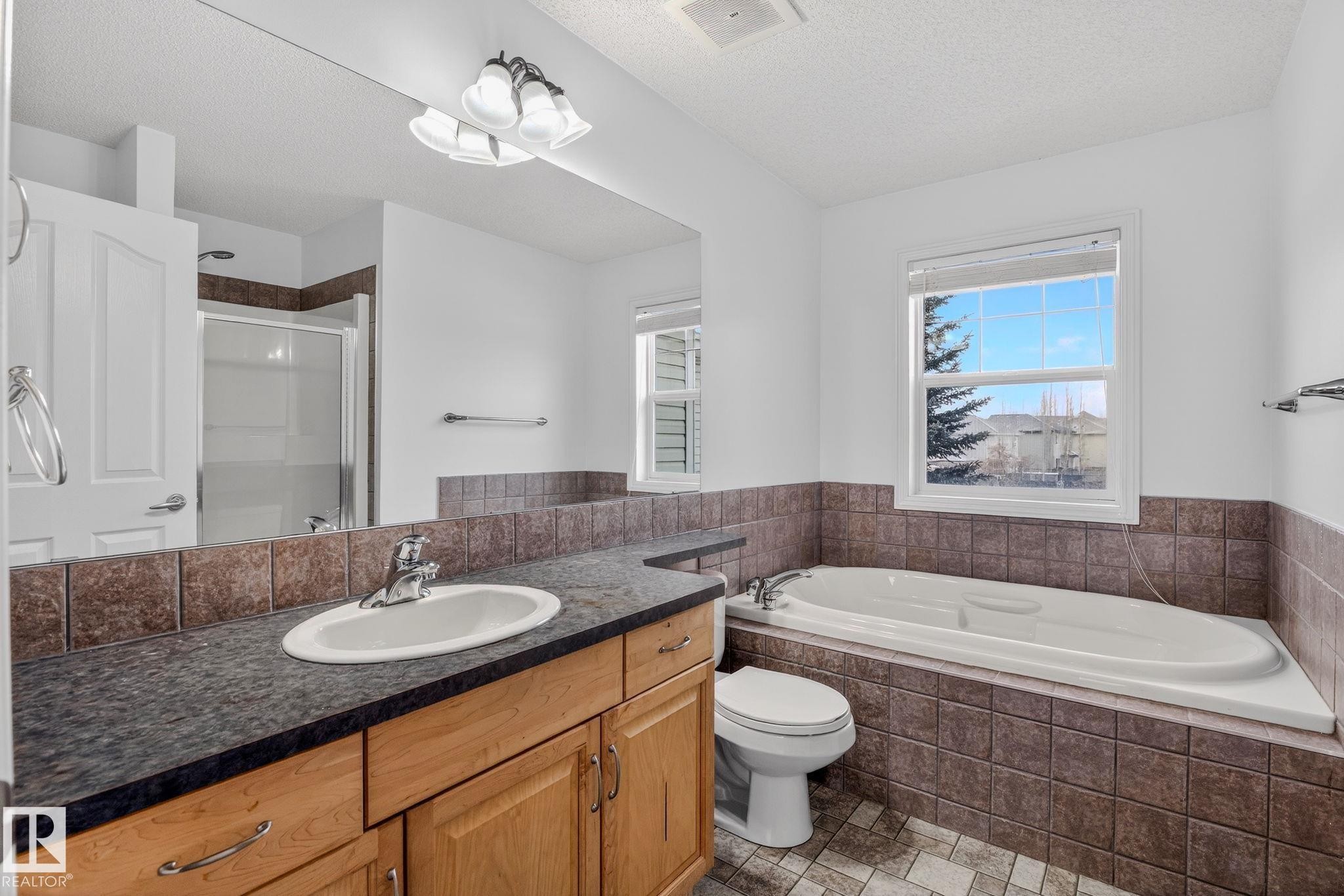 Vanity with wood cabinetry, dark countertop, and integrated oval sink - 978 Rutherford Road Sw, Edmonton, AB - Indoor Photo Showing Bathroom