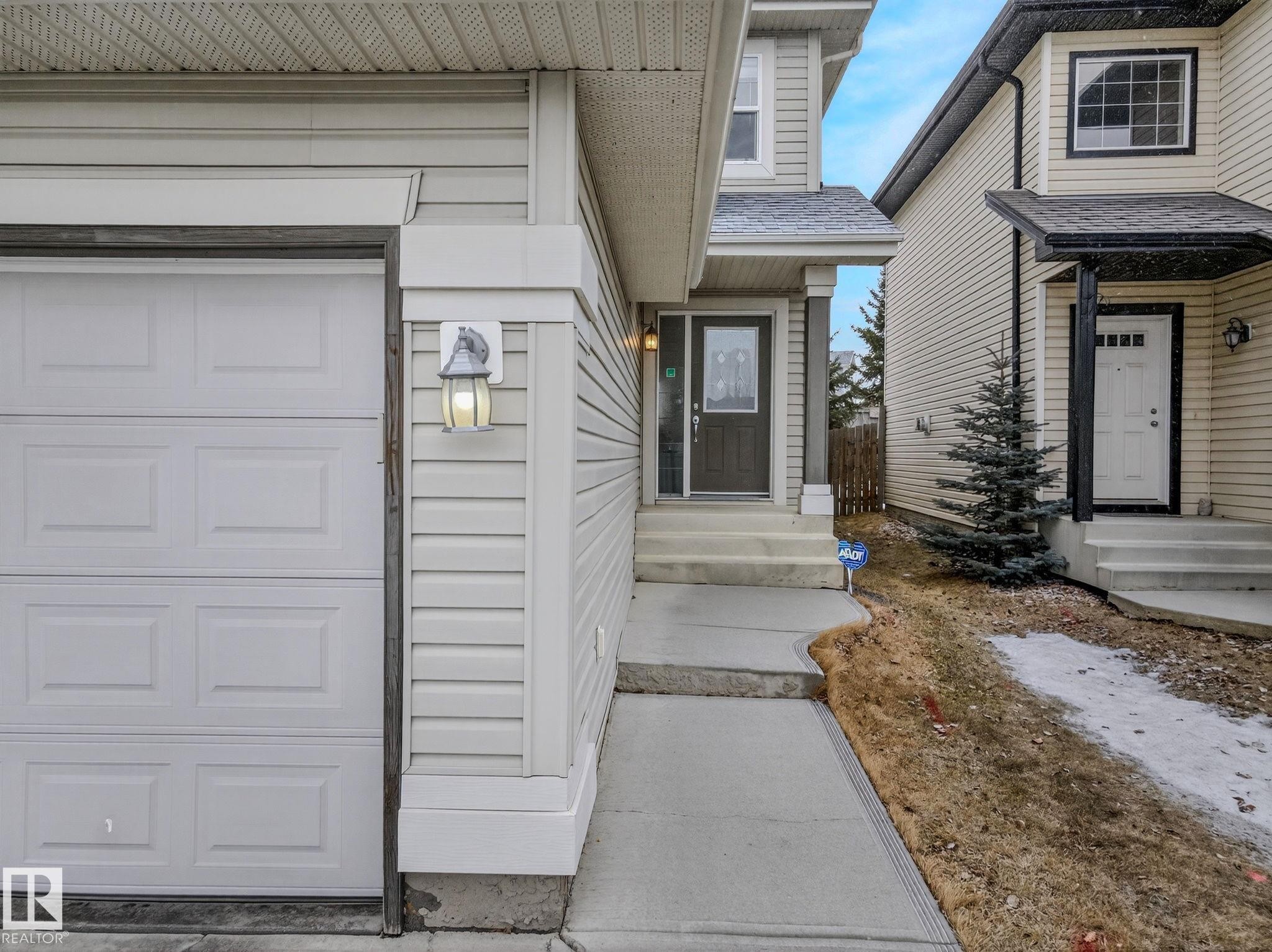 Light-colored siding exterior featuring a paneled garage door and a front entry with a dark door and sidelight - 978 Rutherford Road Sw, Edmonton, AB - Outdoor With Exterior