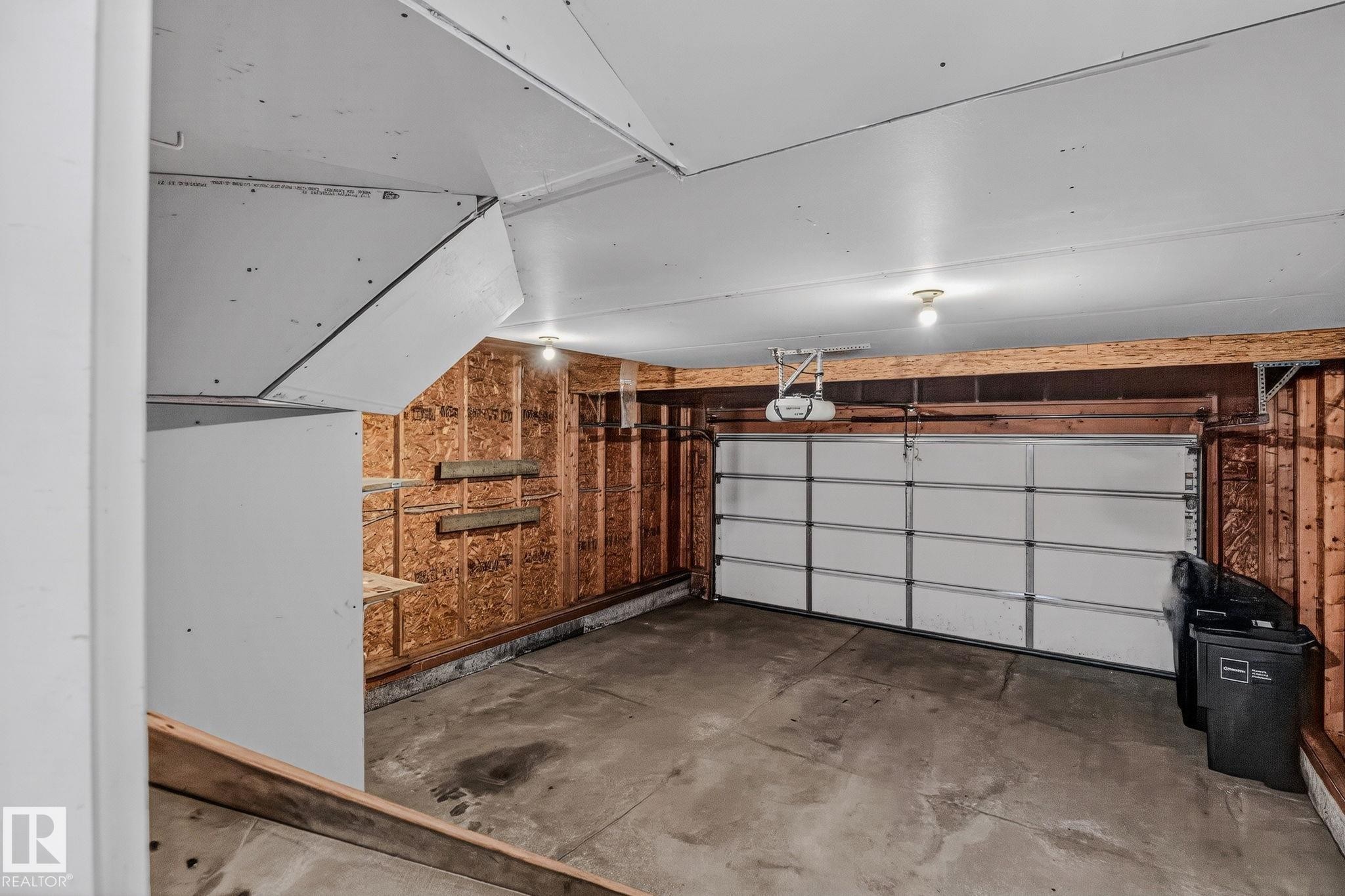 Single-car garage with a paneled overhead door, concrete flooring, and exposed wood framing - 978 Rutherford Road Sw, Edmonton, AB - Indoor Photo Showing Garage