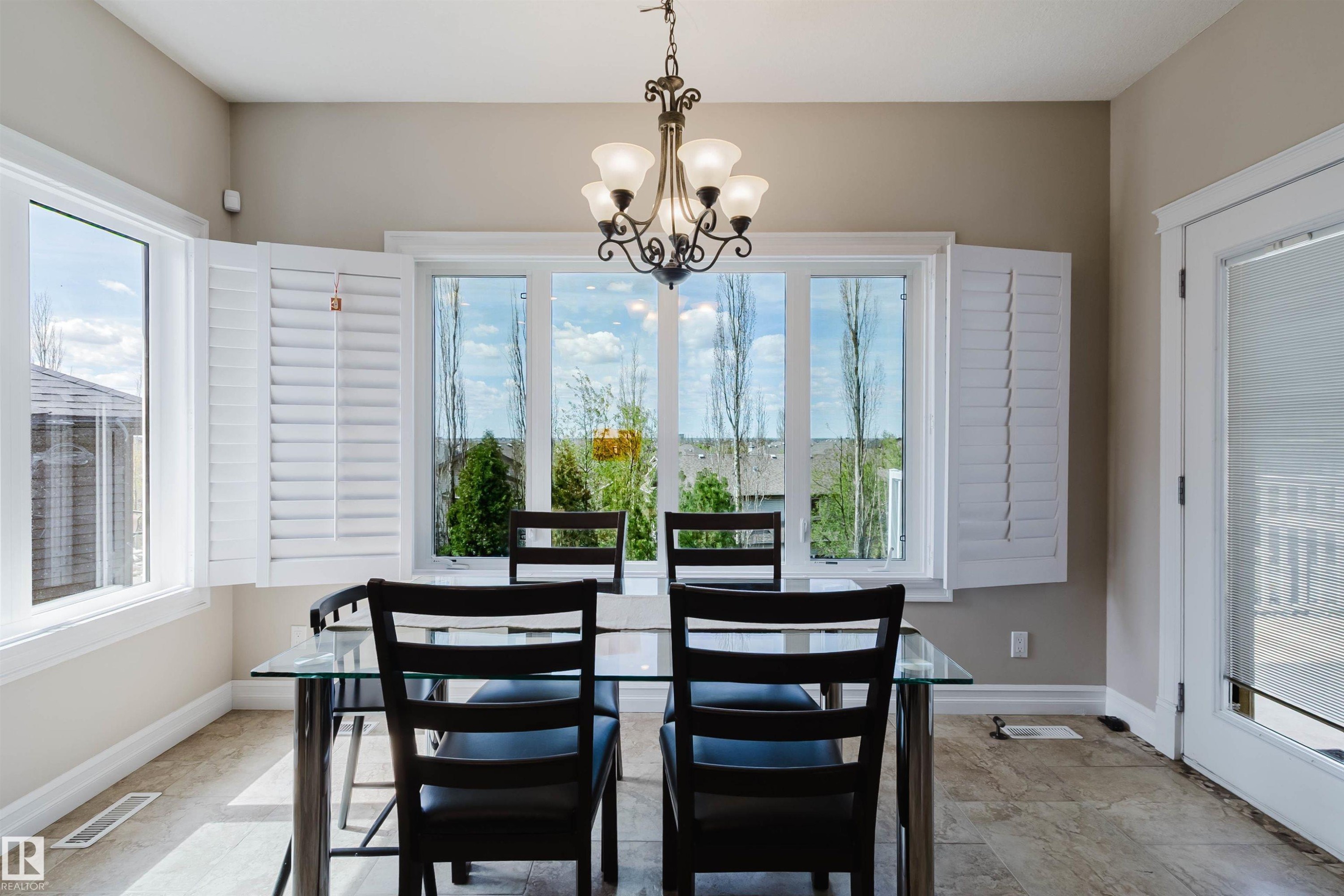 Dining area featuring a prominent window array with plantation shutters, tile flooring, and a decorative chandelier - 3412 Macneil Link, Edmonton, AB - Indoor Photo Showing Dining Room