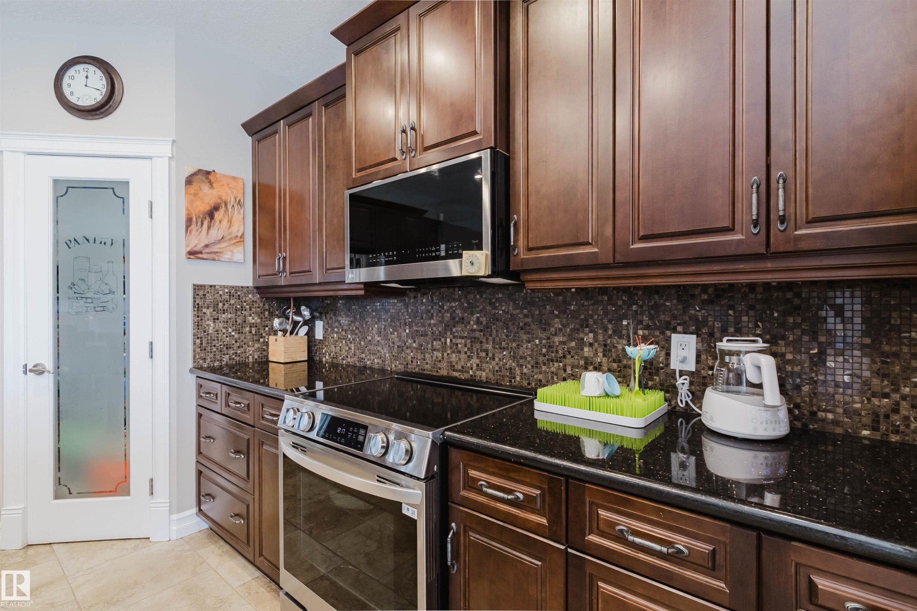 Kitchen featuring dark wood cabinetry, black countertops, a stainless steel range, and a mosaic tile backsplash - 3412 Macneil Link, Edmonton, AB - Indoor Photo Showing Kitchen