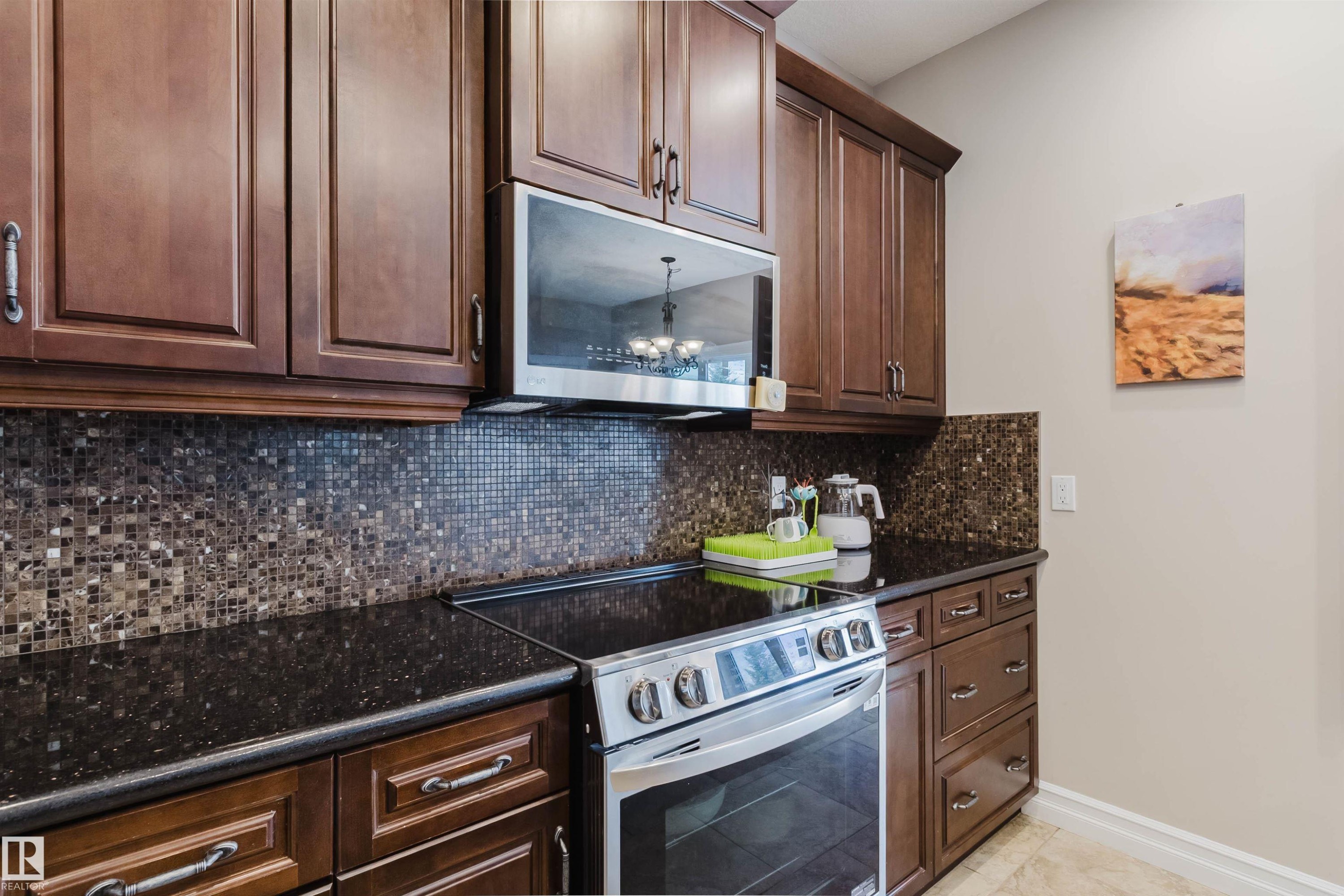 Kitchen featuring rich wood cabinetry, dark speckled countertops, and a mosaic tile backsplash - 3412 Macneil Link, Edmonton, AB - Indoor Photo Showing Kitchen