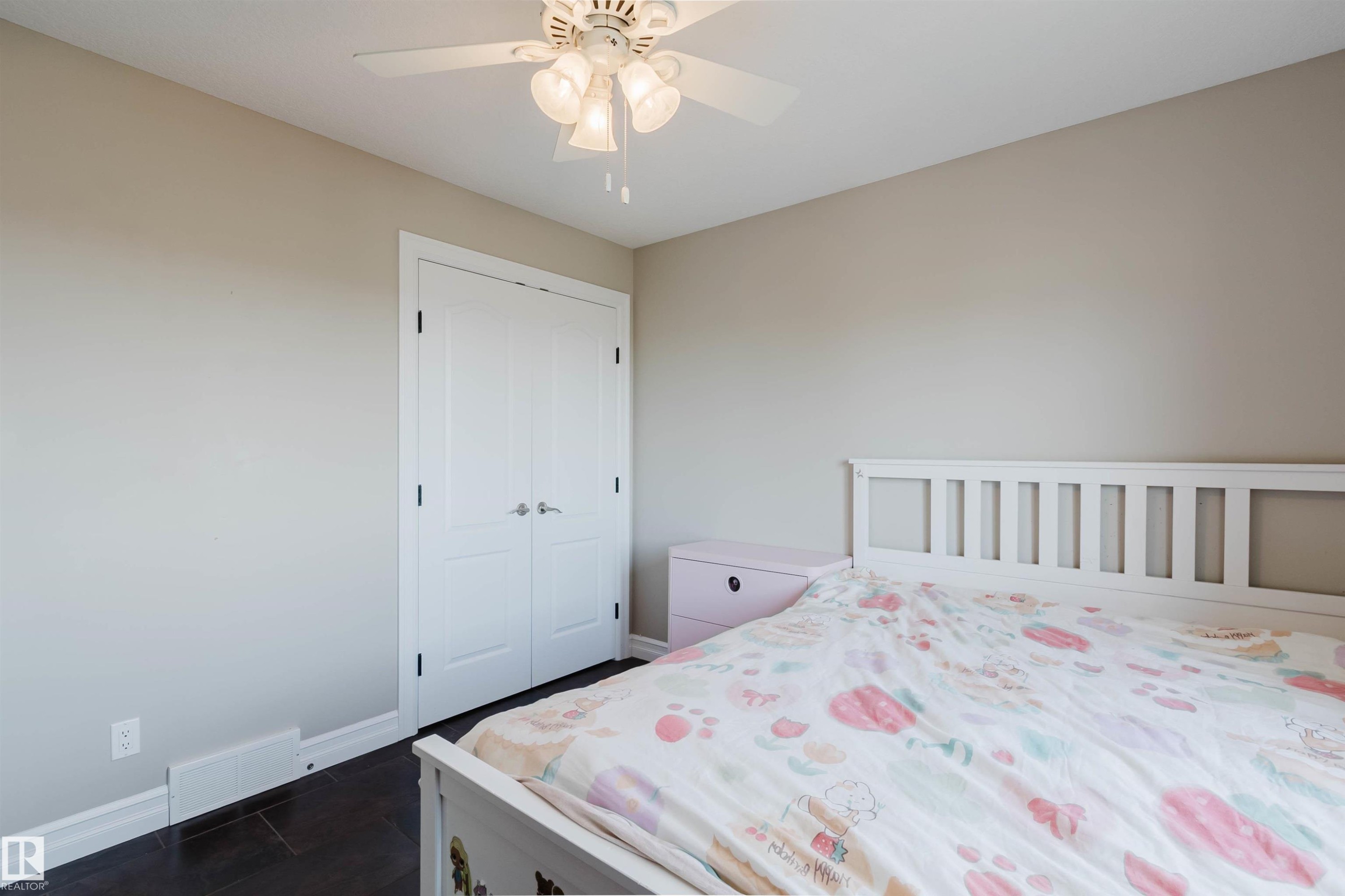 Bedroom featuring a ceiling fan with integrated lighting, a double-door closet with dark hardware, dark wood-finish flooring, and light-toned walls - 3412 Macneil Link, Edmonton, AB - Indoor Photo Showing Bedroom