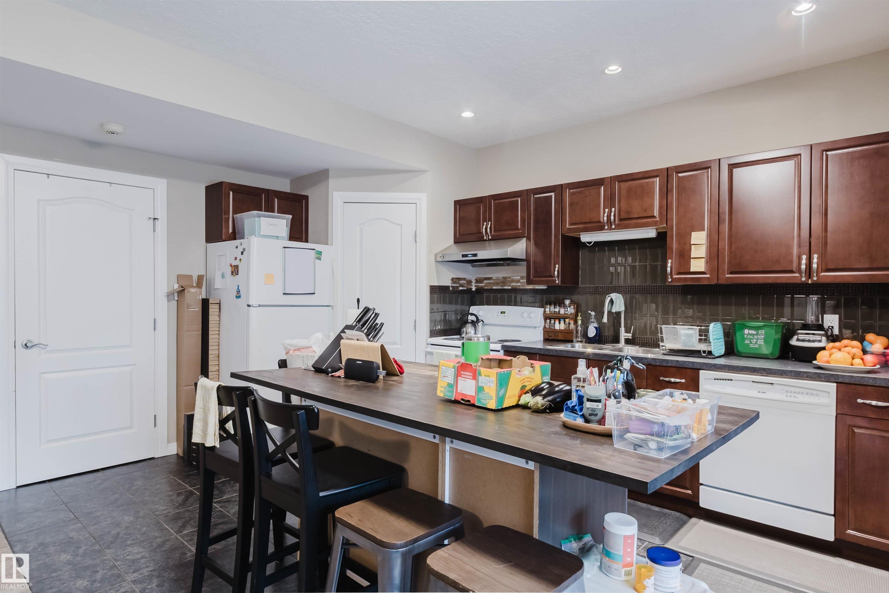 Kitchen featuring dark wood-finish cabinetry, dark tile backsplash, recessed lighting, and a kitchen island with seating - 3412 Macneil Link, Edmonton, AB - Indoor Photo Showing Kitchen