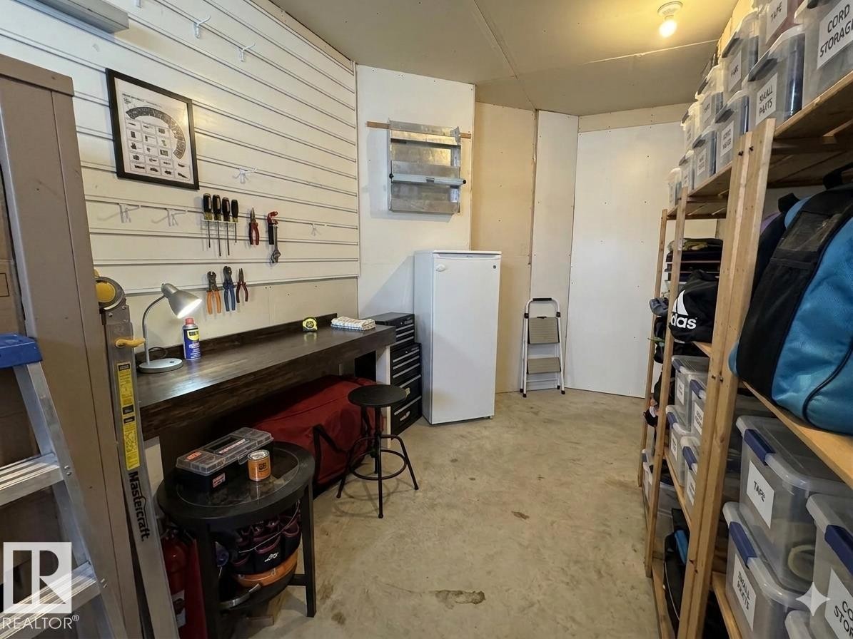 Organized utility room featuring a built-in workbench, wall-mounted storage system, freestanding refrigerator, and extensive shelving units - 3412 Macneil Link, Edmonton, AB - Indoor