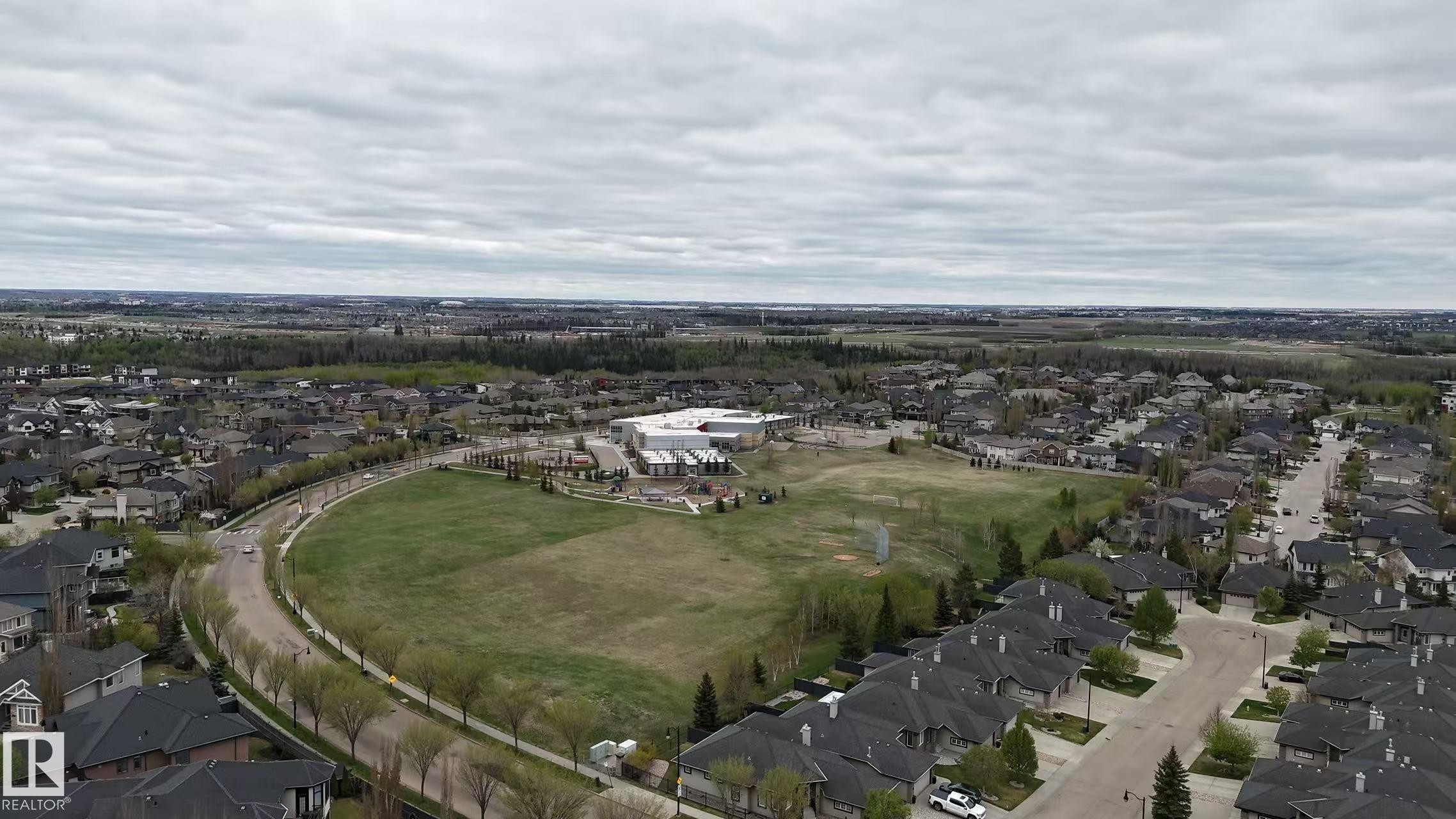 Aerial perspective showcasing a residential development with extensive green space, a school building, and a curvilinear paved road - 3412 Macneil Link, Edmonton, AB - Outdoor With View