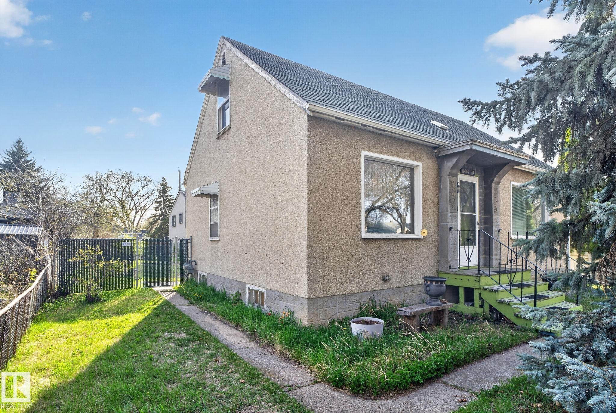 Stucco exterior residence featuring a front entry with green-painted steps and black metal railings - 11614 70 Street, Edmonton, AB