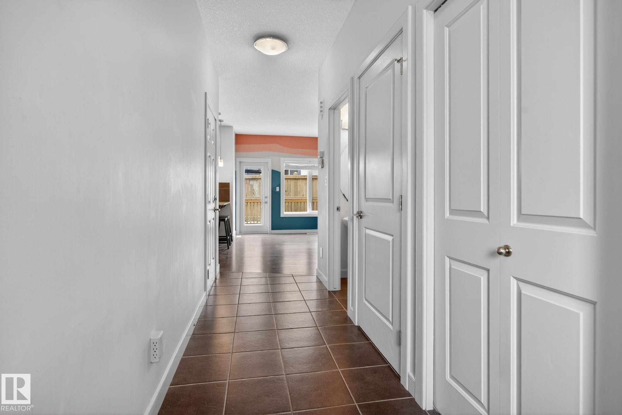 Brown square tile flooring defines a hallway with white paneled doors and walls - 11 450 Mcconachie Way, Edmonton, AB - Indoor Photo Showing Other Room