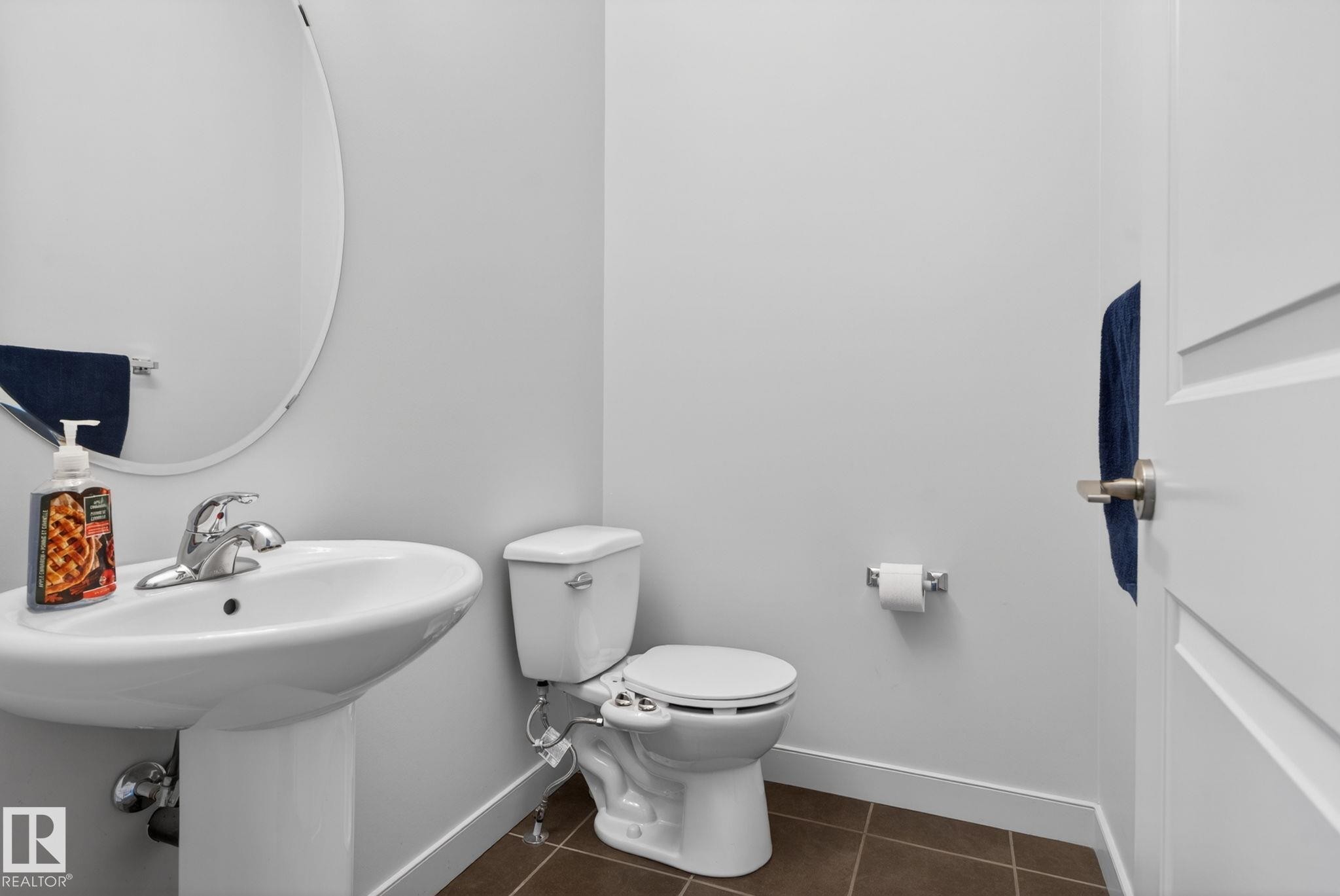 Pedestal sink with chrome faucet, oval wall mirror, and neutral wall paint - 11 450 Mcconachie Way, Edmonton, AB - Indoor Photo Showing Bathroom