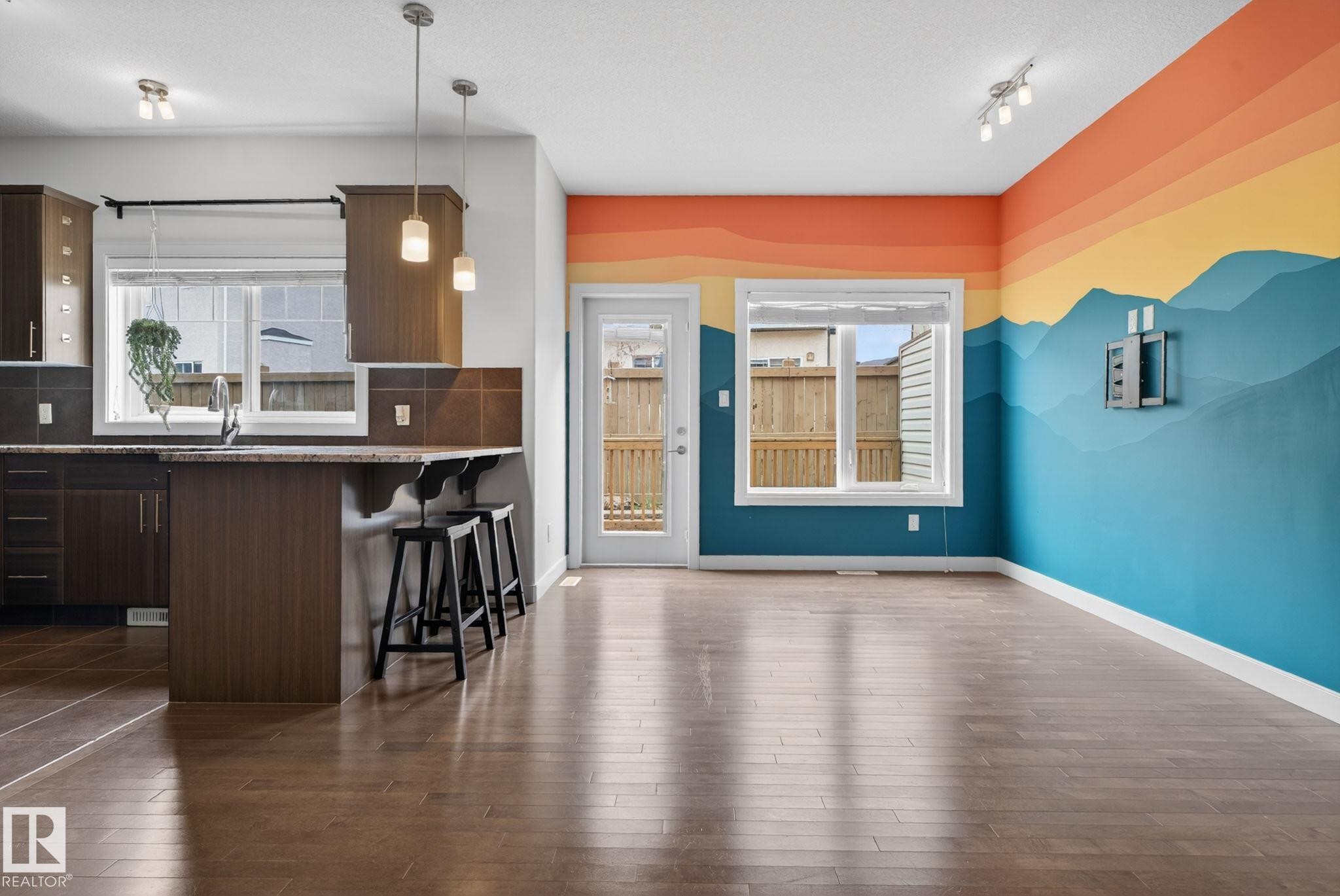 Open-concept living area featuring wood-finish flooring, a kitchen island with seating, pendant lighting, and a rear patio door - 11 450 Mcconachie Way, Edmonton, AB - Indoor