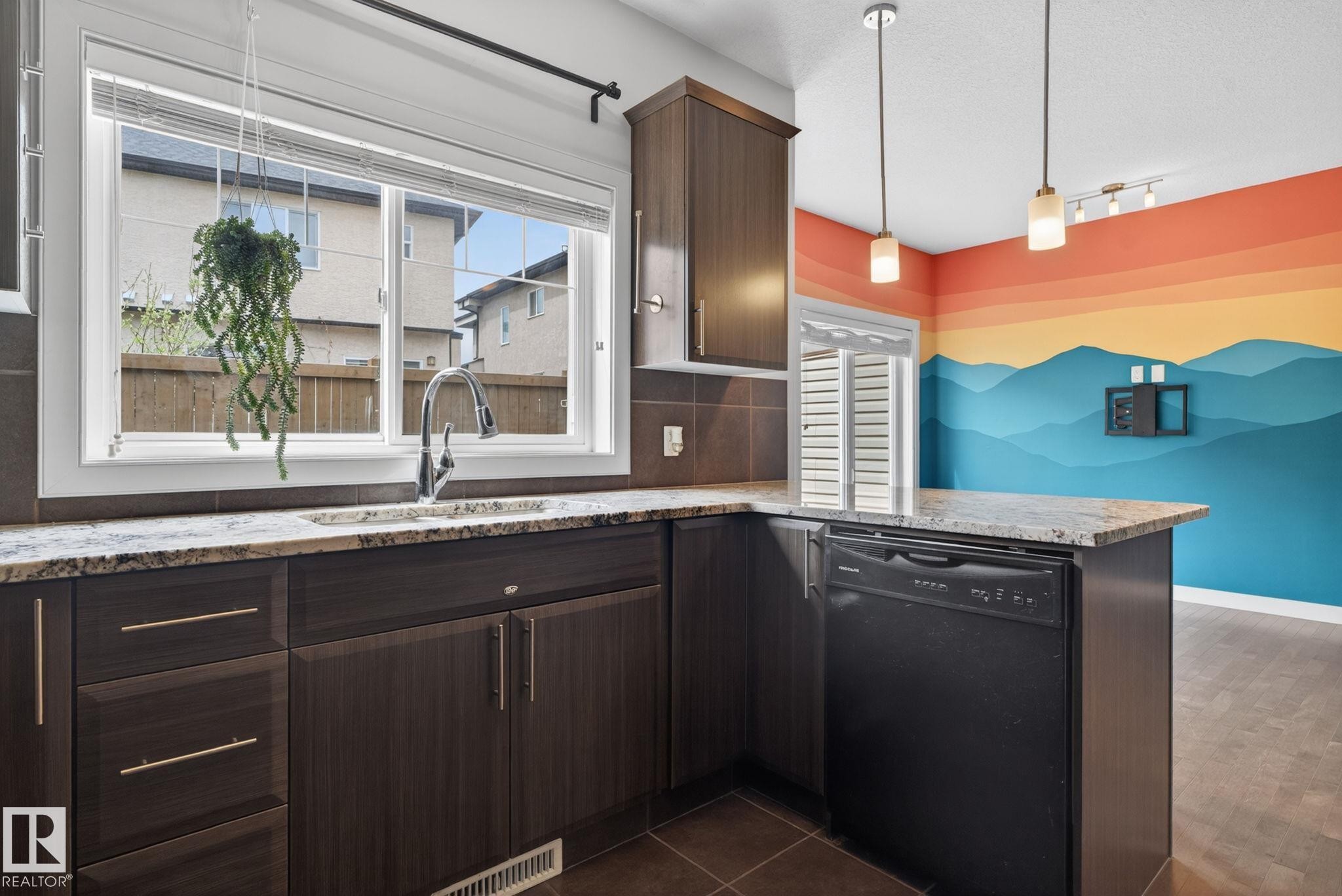 Kitchen featuring dark wood-finish cabinetry, light-toned granite countertops, a stainless steel faucet, and an integrated black dishwasher - 11 450 Mcconachie Way, Edmonton, AB - Indoor