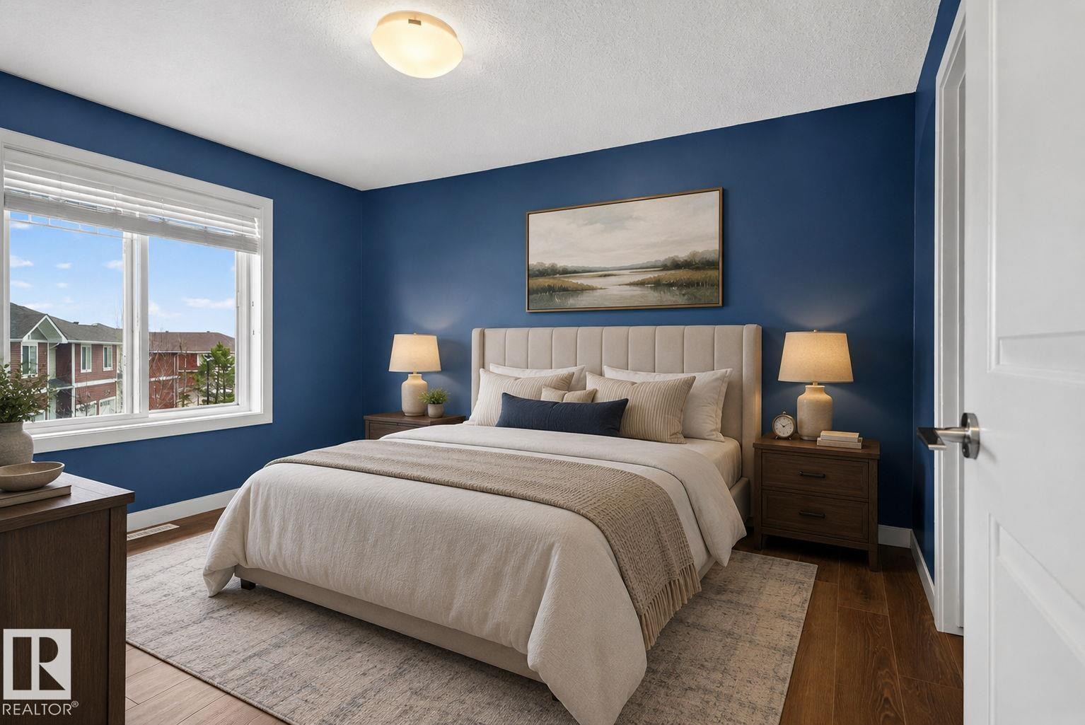 Spacious room featuring wood-finish flooring, a large window with white trim, and a contemporary ceiling light fixture - 11 450 Mcconachie Way, Edmonton, AB - Indoor Photo Showing Bedroom