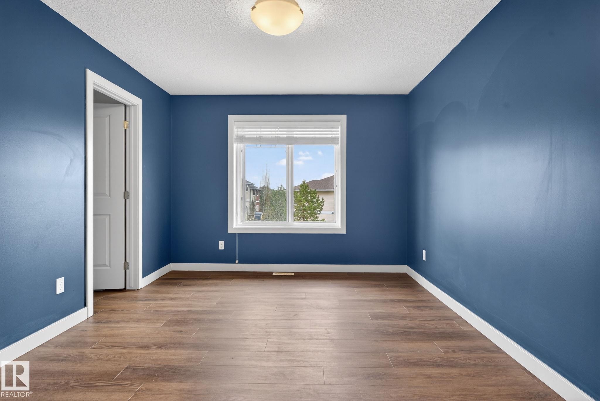 Room featuring wood-finish flooring, a window with white trim, and a white interior door - 11 450 Mcconachie Way, Edmonton, AB - Indoor Photo Showing Other Room