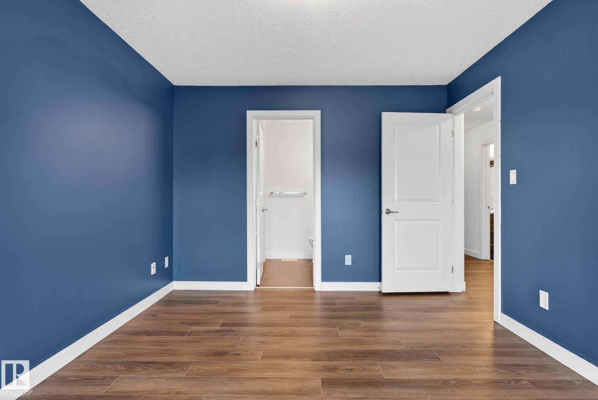 Interior room featuring rich blue wall paint, wood-finish flooring, white baseboards, and white two-panel interior doors - 11 450 Mcconachie Way, Edmonton, AB - Indoor Photo Showing Other Room