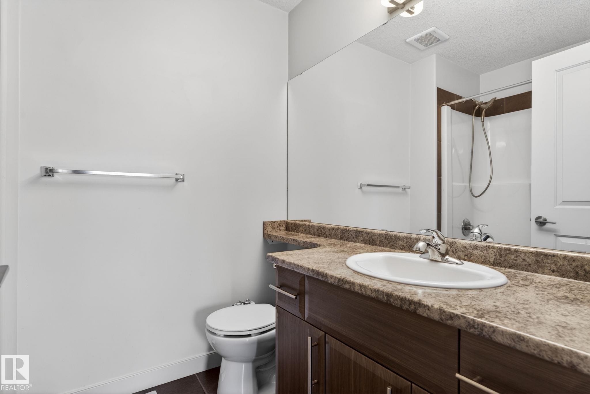 Bathroom featuring a wood-finish vanity with a built-in sink, a speckled countertop, a large wall mirror, and a shower-tub combination - 11 450 Mcconachie Way, Edmonton, AB - Indoor Photo Showing Bathroom