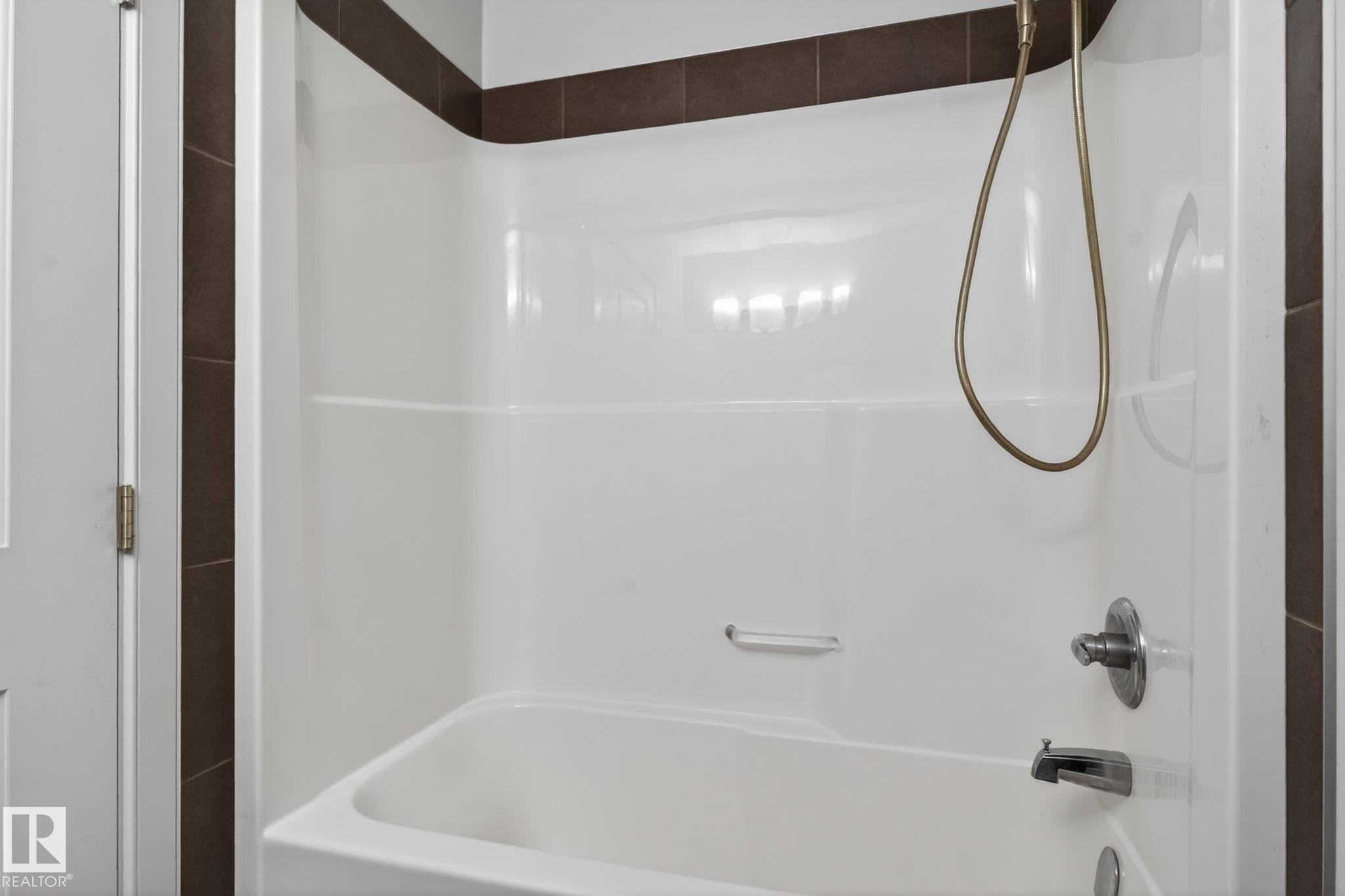 White tub-shower combination unit featuring integrated shelving, a brushed nickel faucet, and a handheld shower head - 11 450 Mcconachie Way, Edmonton, AB - Indoor Photo Showing Bathroom