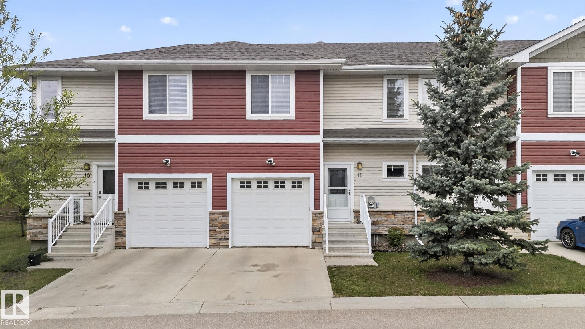 Townhome exterior featuring red and beige horizontal siding, a gabled roofline, and white-framed windows - 11 450 Mcconachie Way, Edmonton, AB - Outdoor With Facade