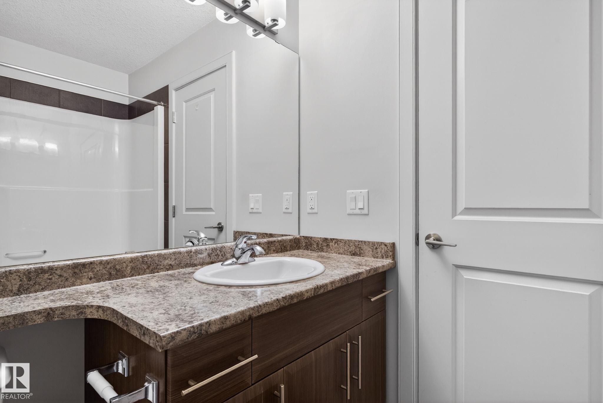 Bathroom featuring a dark wood-finish vanity with an integrated sink, a speckled countertop, and a large wall-mounted mirror - 11 450 Mcconachie Way, Edmonton, AB - Indoor Photo Showing Bathroom