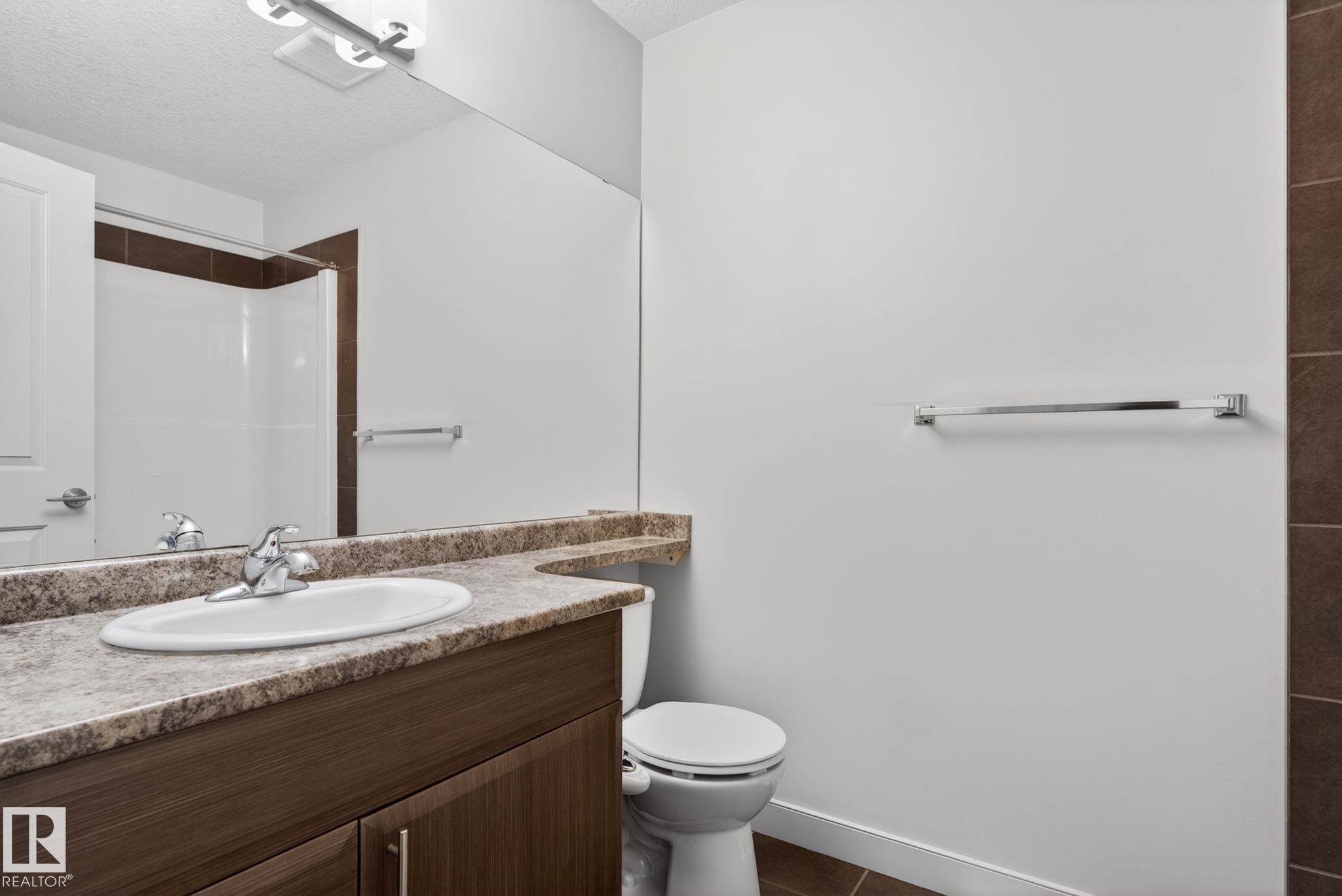 Bathroom featuring a wood-finish vanity with an integrated sink and a speckled countertop - 11 450 Mcconachie Way, Edmonton, AB - Indoor Photo Showing Bathroom