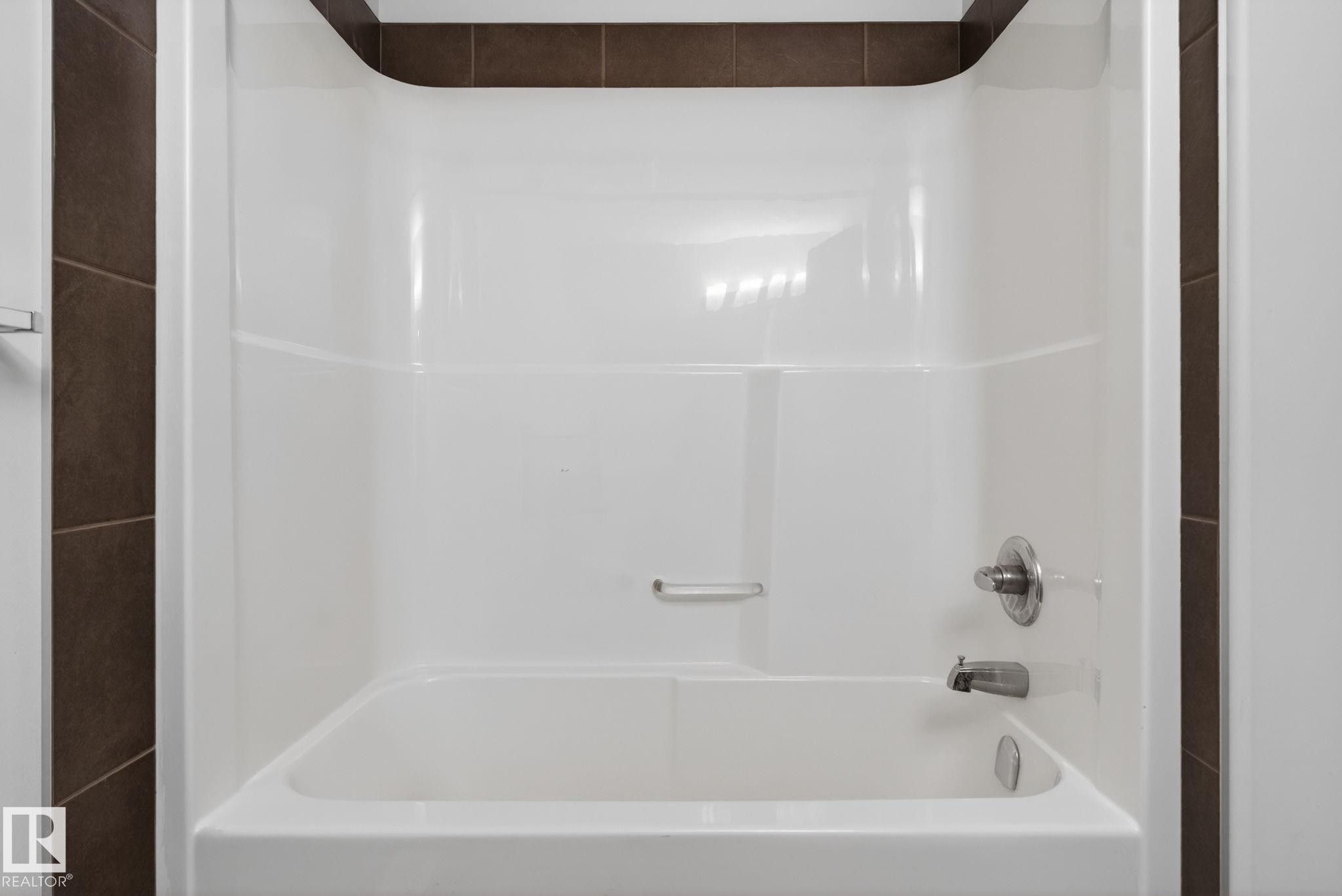 White acrylic tub and shower combination with chrome fixtures, complemented by dark brown tile surround - 11 450 Mcconachie Way, Edmonton, AB - Indoor Photo Showing Bathroom
