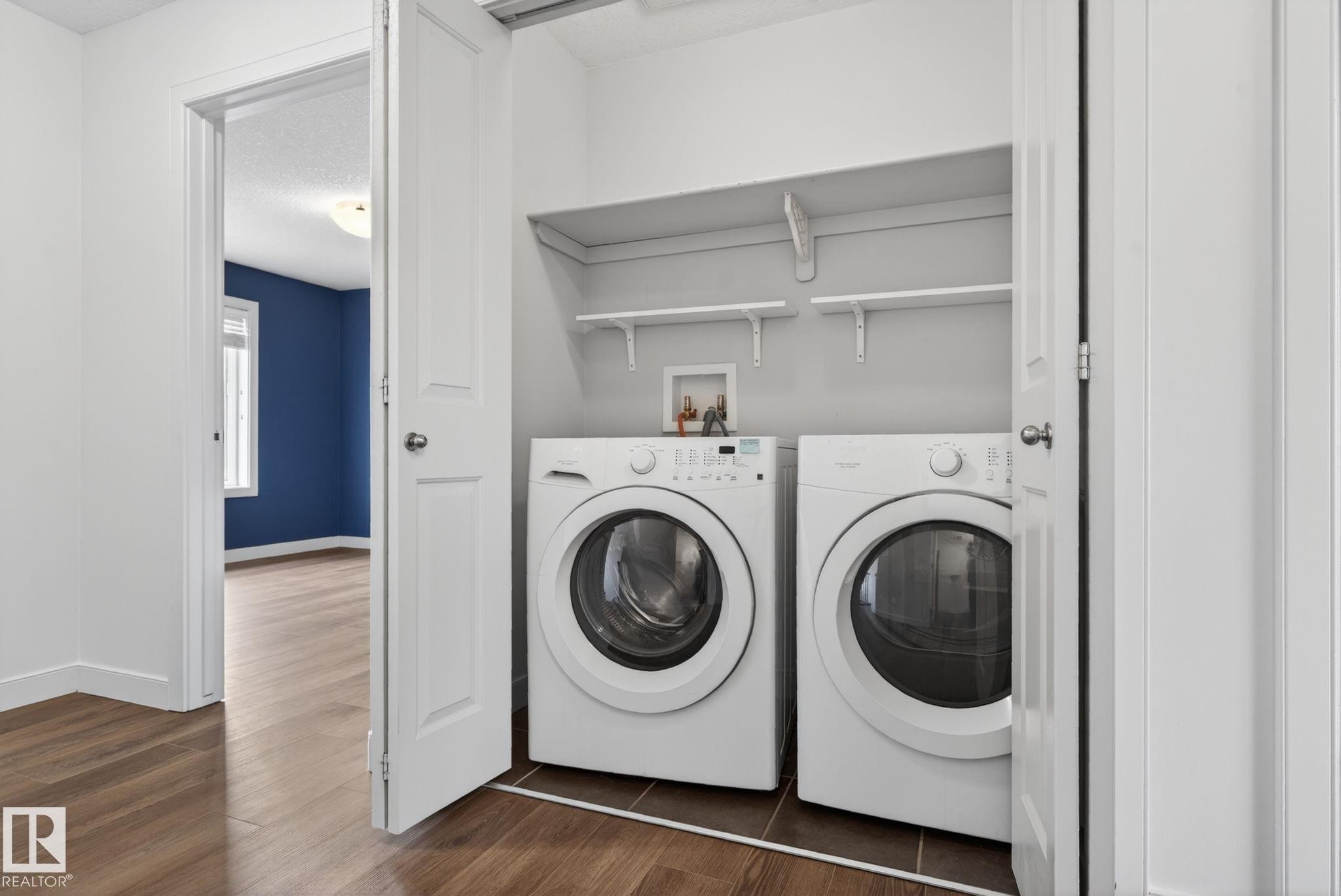 Dedicated laundry closet featuring a white front-load washer and dryer, integrated shelving, and a durable tile floor - 11 450 Mcconachie Way, Edmonton, AB - Indoor Photo Showing Laundry Room