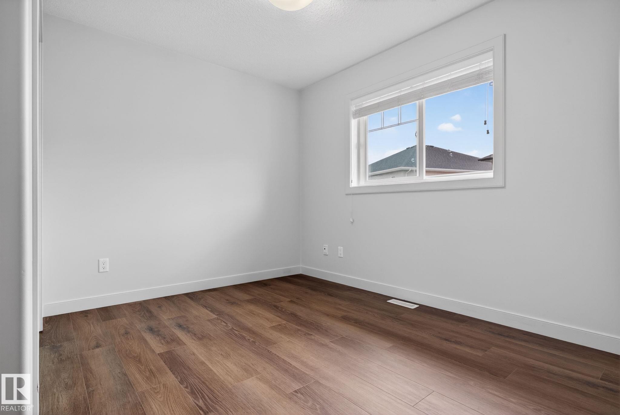 Room featuring wood-finish flooring, white baseboards, a white window frame, and a ceiling-mounted light fixture - 11 450 Mcconachie Way, Edmonton, AB - Indoor Photo Showing Other Room
