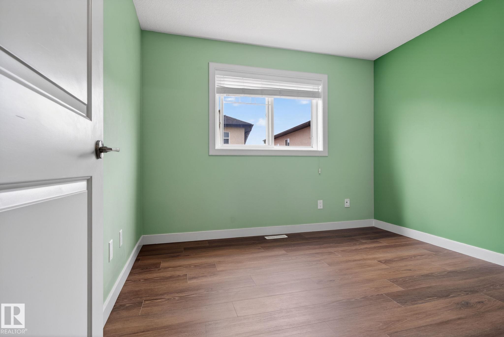 Bright room featuring green painted walls, white trim, wood-finish flooring, and a window with blinds - 11 450 Mcconachie Way, Edmonton, AB - Indoor Photo Showing Other Room