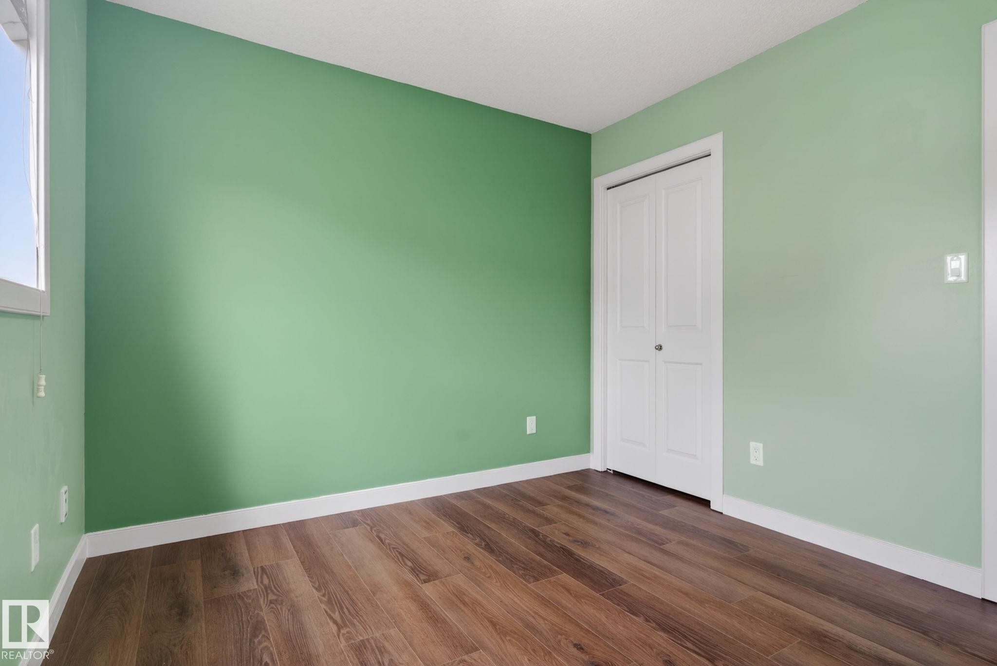 Interior room featuring wood-finish flooring, white baseboards, and a bi-fold closet door - 11 450 Mcconachie Way, Edmonton, AB - Indoor Photo Showing Other Room