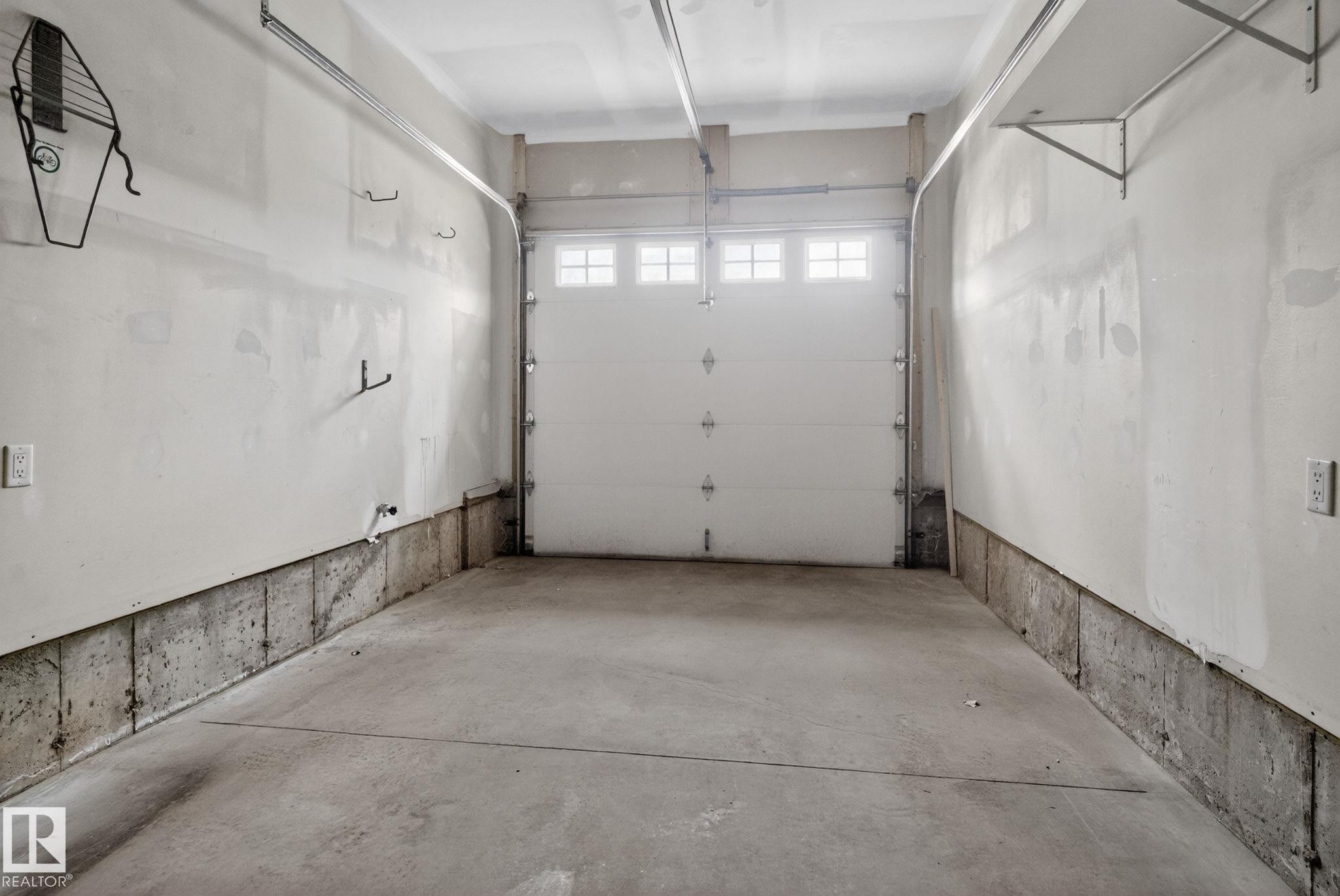 Spacious garage featuring a concrete floor, painted white walls, and a white overhead door with windows - 11 450 Mcconachie Way, Edmonton, AB - Indoor Photo Showing Garage