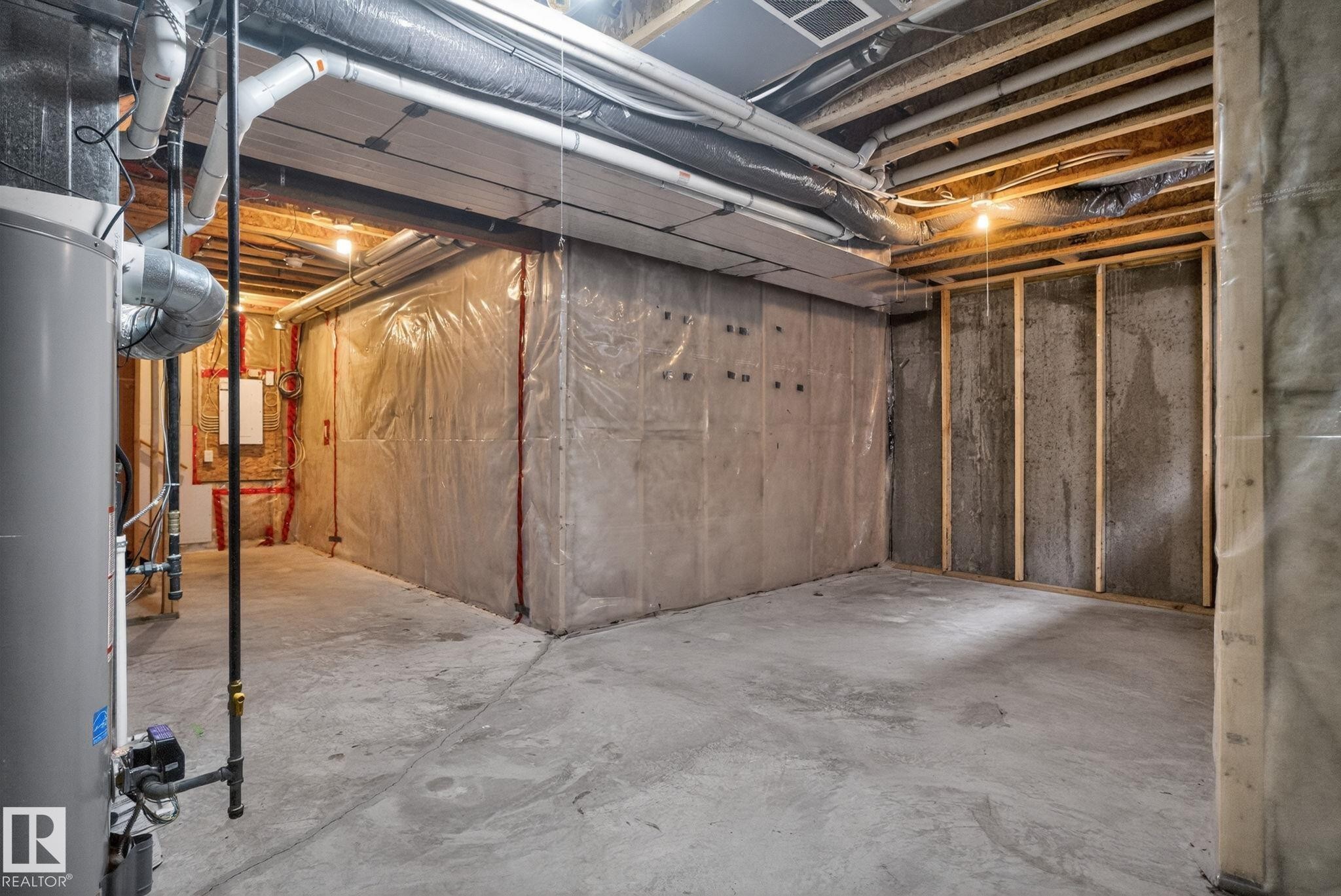 Unfinished basement featuring exposed wood joists, concrete flooring, foundational walls, and a water heater - 11 450 Mcconachie Way, Edmonton, AB - Indoor Photo Showing Basement