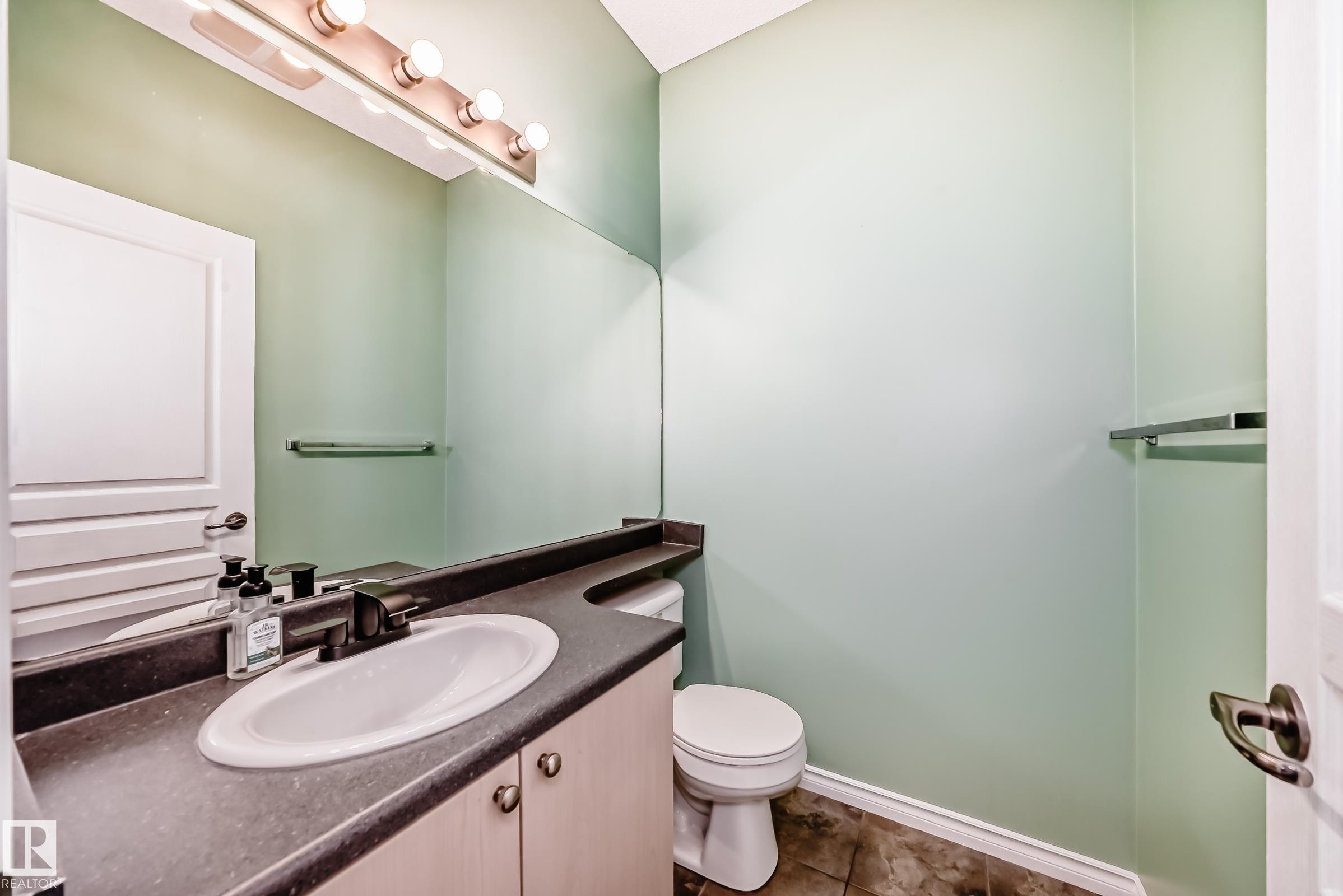 Bathroom featuring a vanity with an oval sink, dark countertop, and light wood-finish cabinetry - 105 13825 155 Avenue, Edmonton, AB - Indoor Photo Showing Bathroom