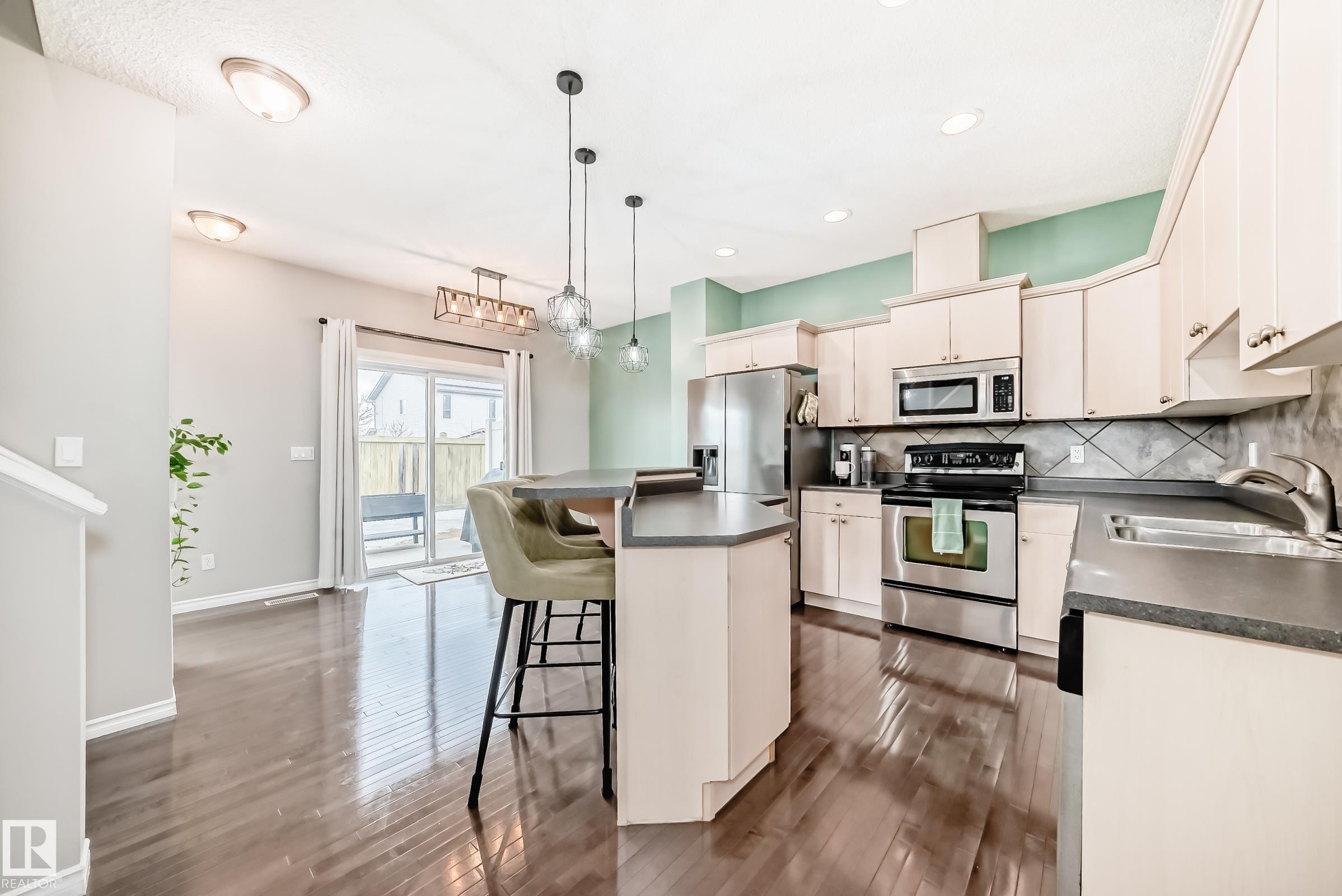 Kitchen featuring stainless steel appliances, dark countertops, light cabinetry, and a textured tile backsplash - 105 13825 155 Avenue, Edmonton, AB - Indoor Photo Showing Kitchen With Stainless Steel Kitchen