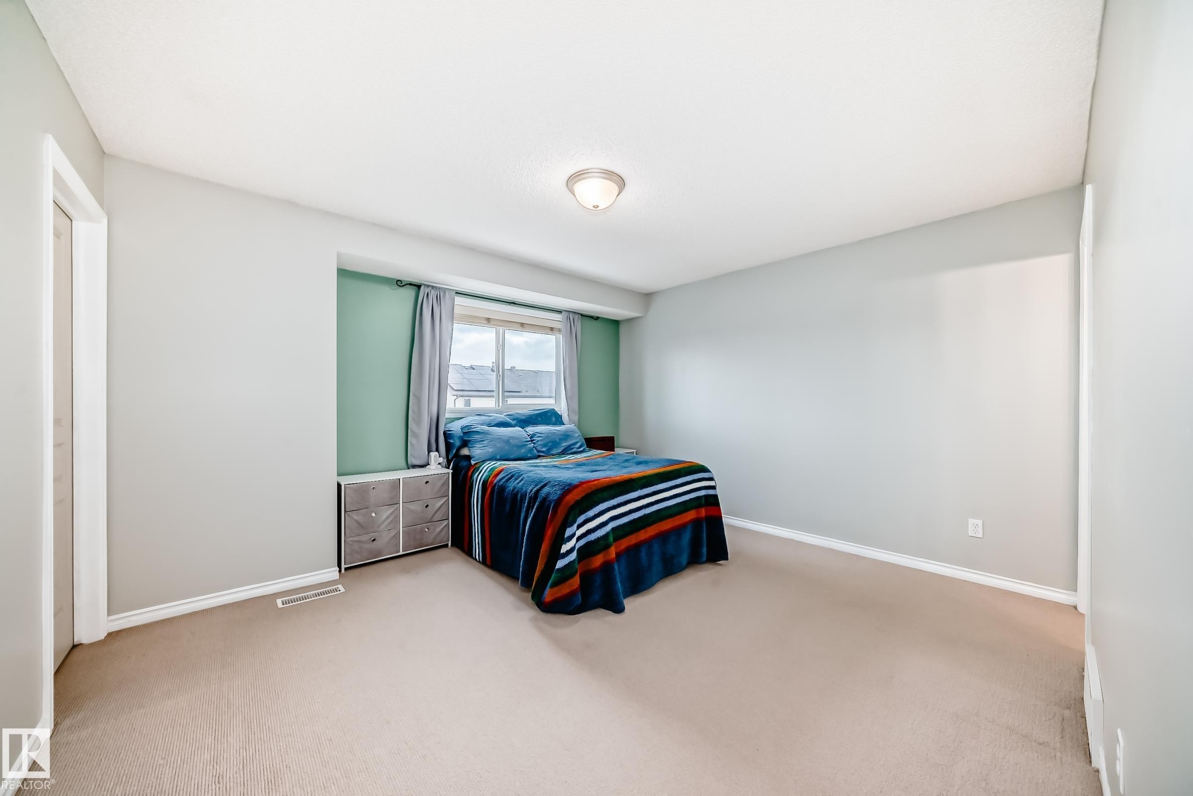Carpeted room with light gray walls, a window with a green accent wall, and white baseboards - 105 13825 155 Avenue, Edmonton, AB - Indoor Photo Showing Bedroom