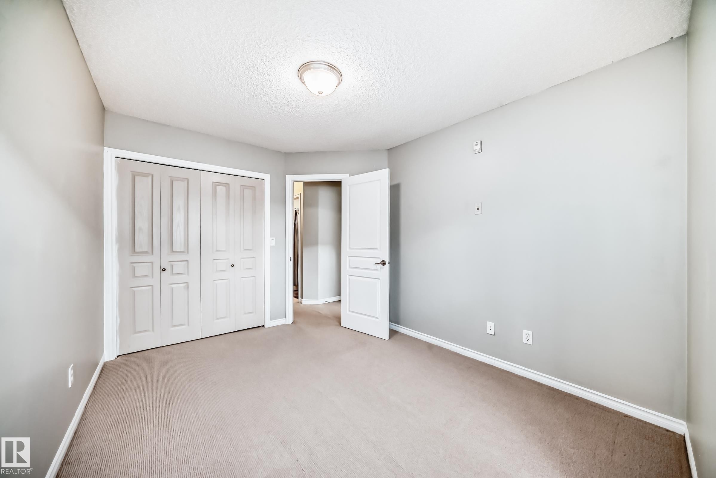 Neutral-toned room featuring a textured ceiling, flush-mount lighting, and light gray wall paint - 105 13825 155 Avenue, Edmonton, AB - Indoor Photo Showing Other Room