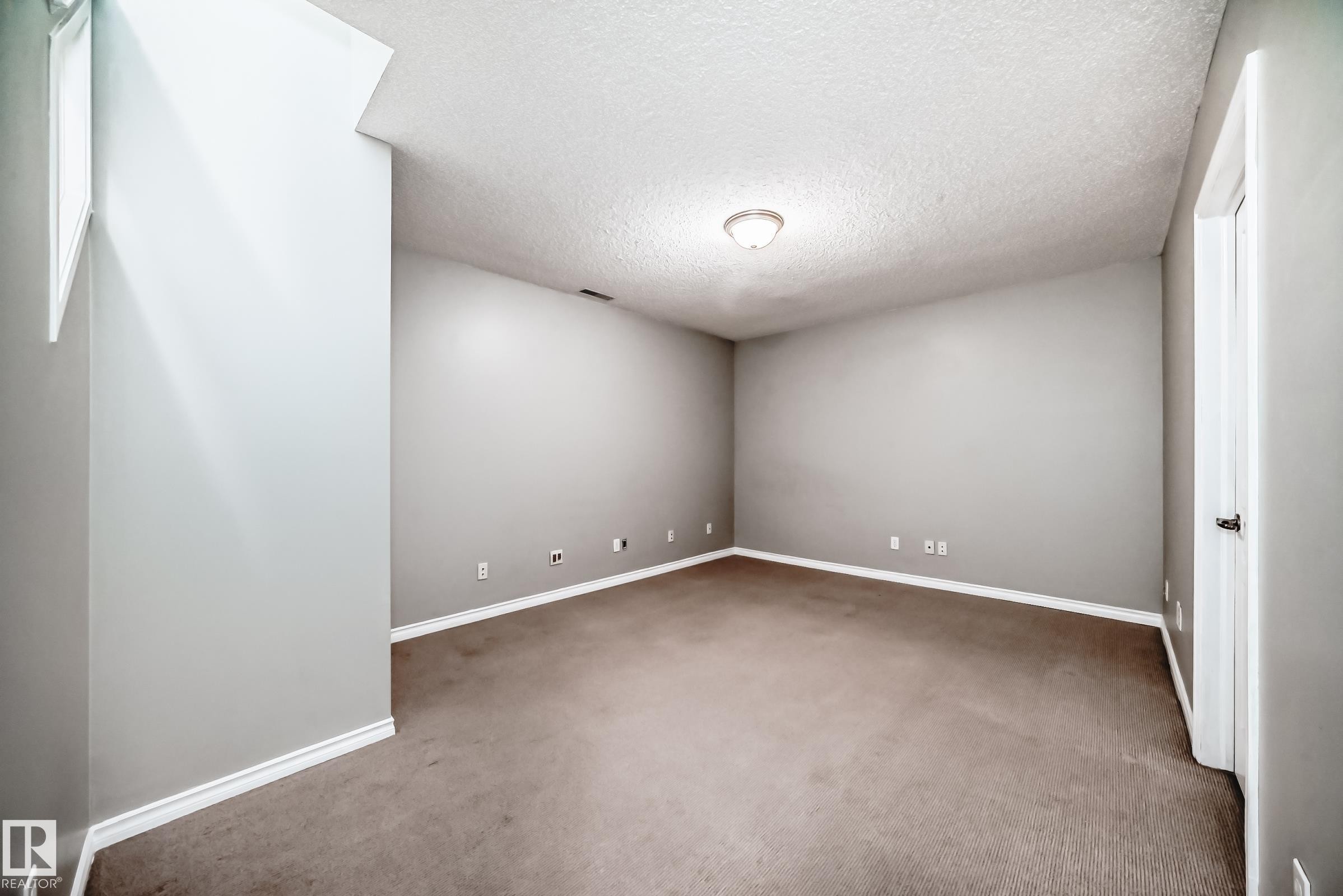 Spacious room featuring neutral grey walls, textured ceiling, and brown carpet flooring - 105 13825 155 Avenue, Edmonton, AB - Indoor Photo Showing Other Room