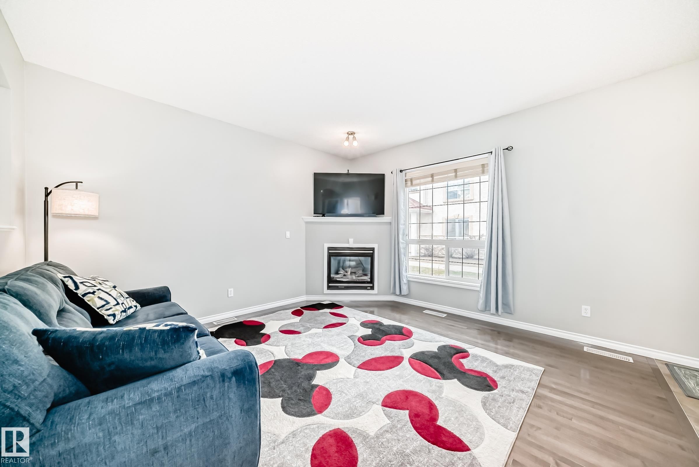 Living area featuring vaulted ceilings, a corner fireplace with mantle, wood-finish flooring, and a large window with white muntins - 105 13825 155 Avenue, Edmonton, AB - Indoor Photo Showing Living Room With Fireplace